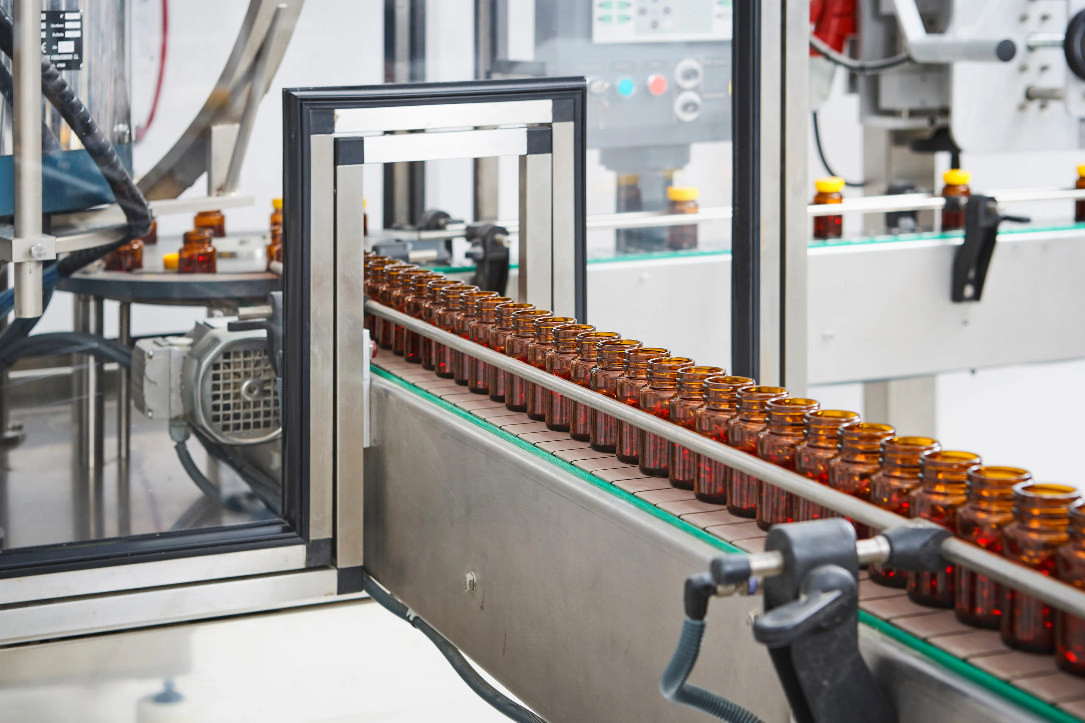 Assembly line in factory glass vials being filled with pills and tablets