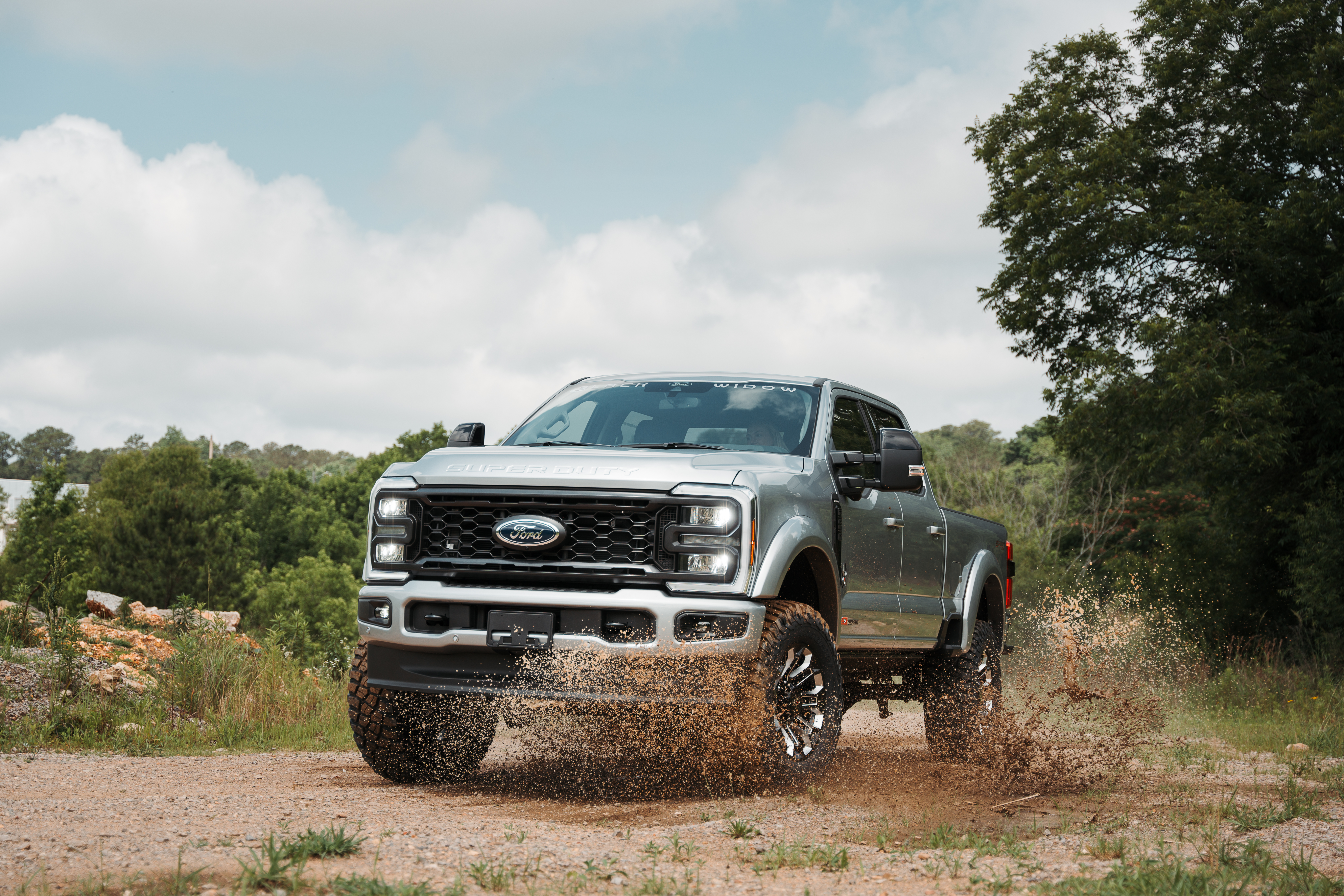 Silver Ford f150 Lifted Black widow Limited Truck offroading and splashing through a mud puddle