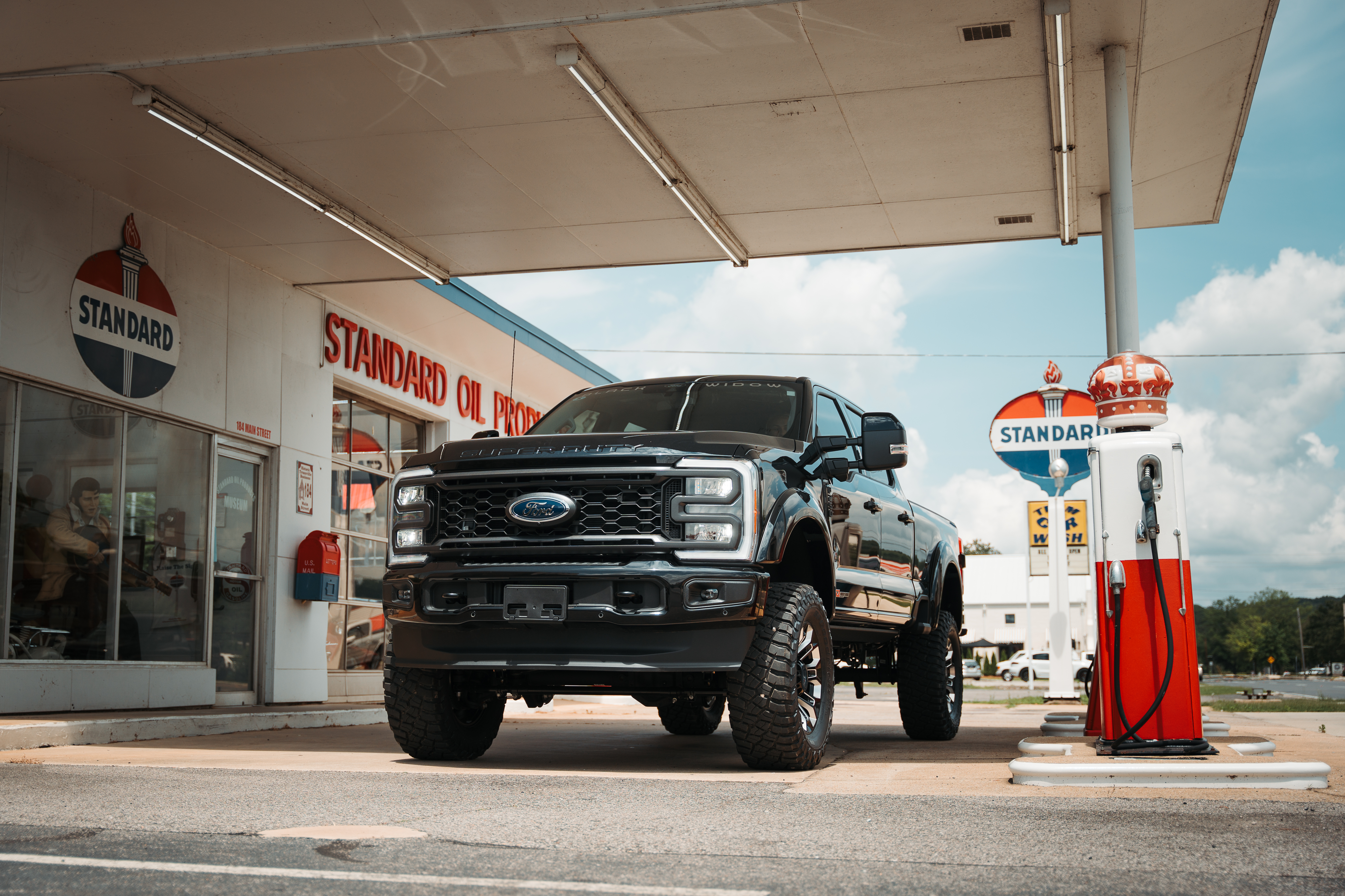 Black Ford f150 Lifted Black Widow Truck parked at a classic Standard Gas station