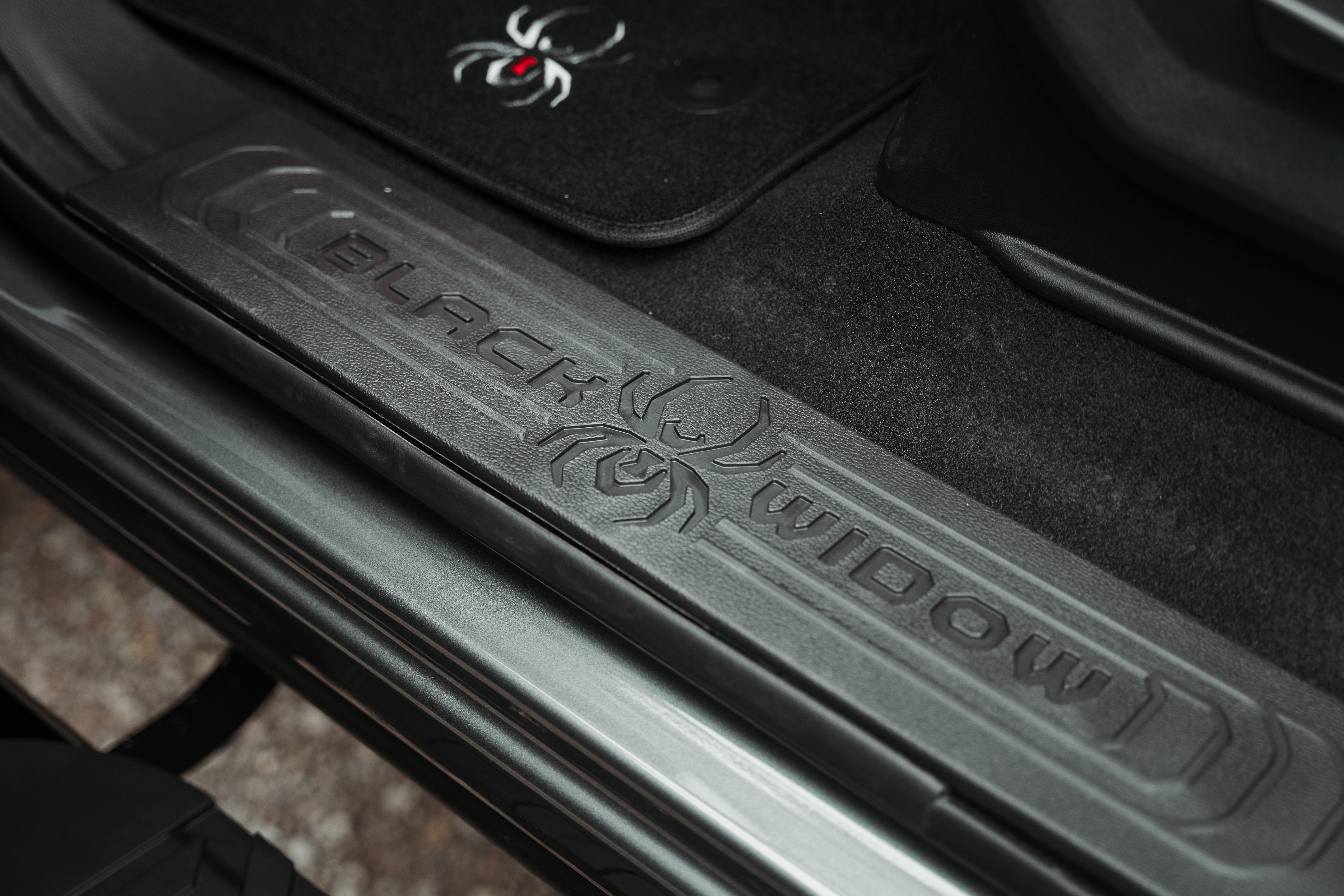 black widow spyder logo embossed door sills and removable embroidered floor mats inside the cab of a black widow lifted truck