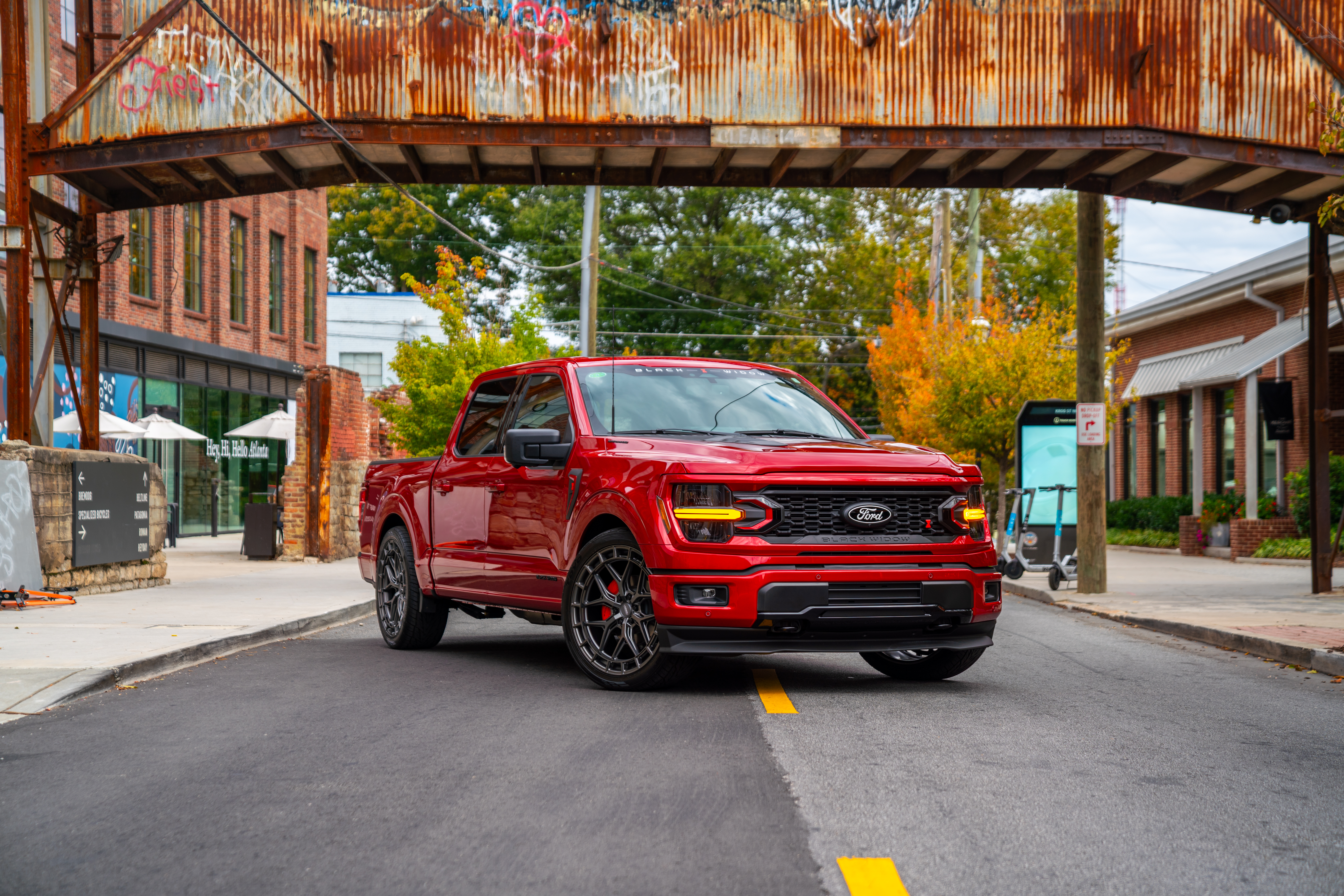 Red ford f150 lowered black widow sr truck on a city street below a rusty bridge headlights on and red accents on the custom black widow grille