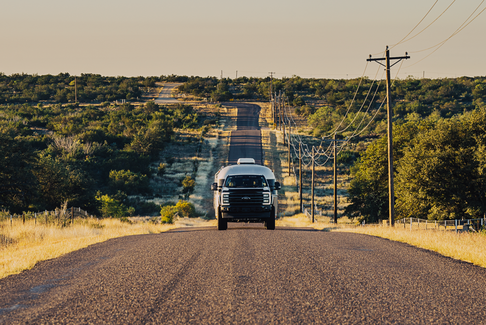 Lifted f250 ford superduty towing a large silver air stream up a hill on a road lined by power lines