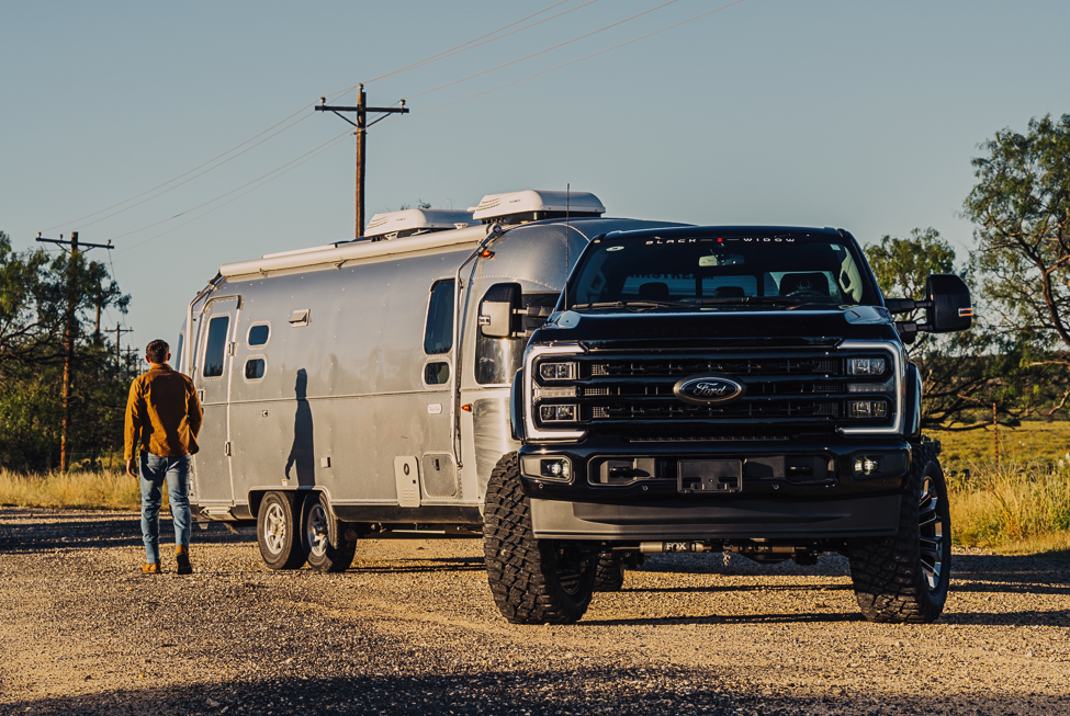 black widow superduty ford lifted f250 truck with headlights on towing a large silver airstream