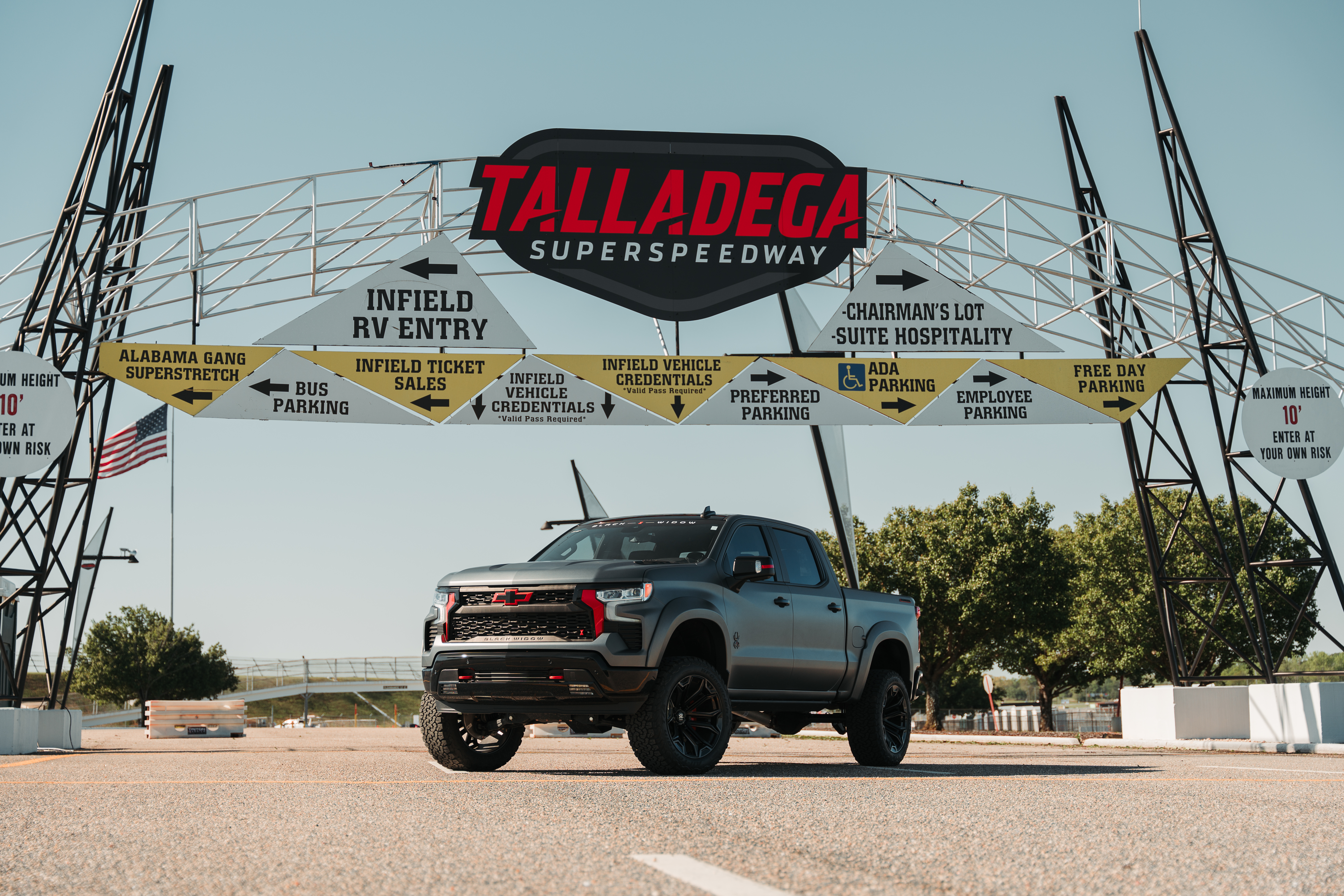 matte silver grey and black hi hat chevvrolet silverado black widow limited lifted truck with red accents and custom grille parked outside of talladega superspeedway