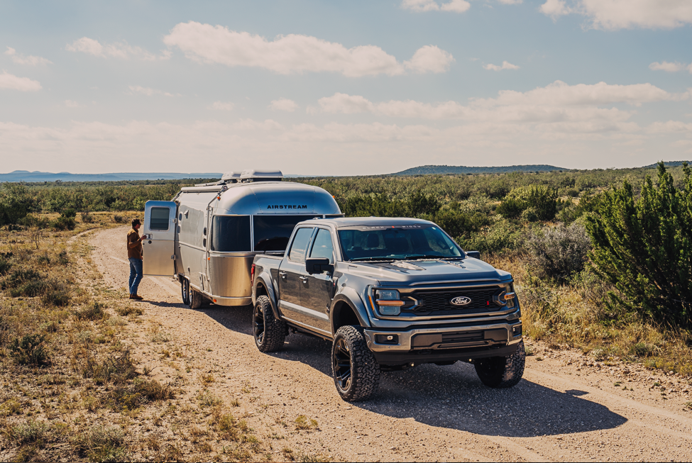 silver black widow ford f150 lifted truck with a small silver air stream ready to tow. Hooked up to the bed of the truck and the door is open