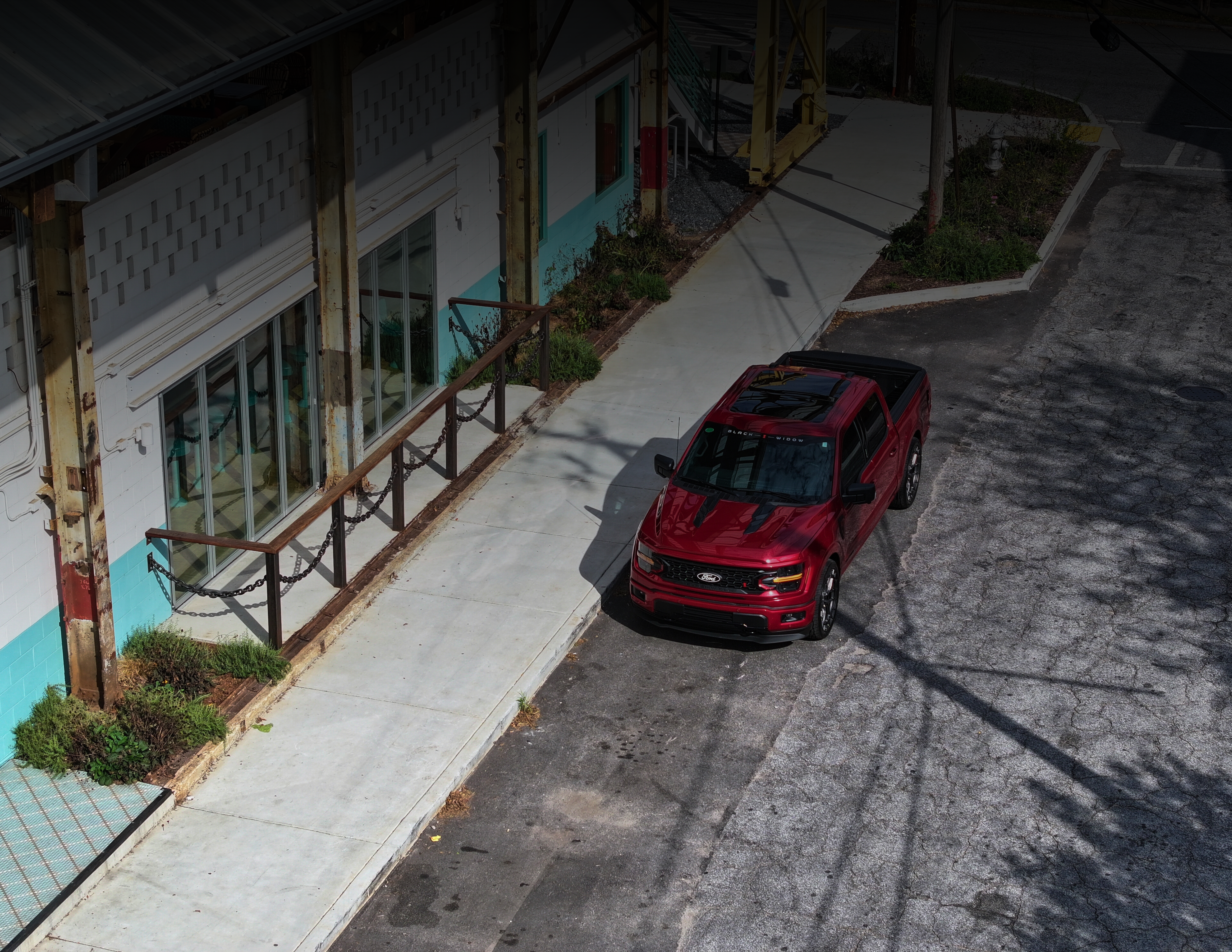 drone shot of a red lowered black widow f150 sr. parked outside of a industrial building