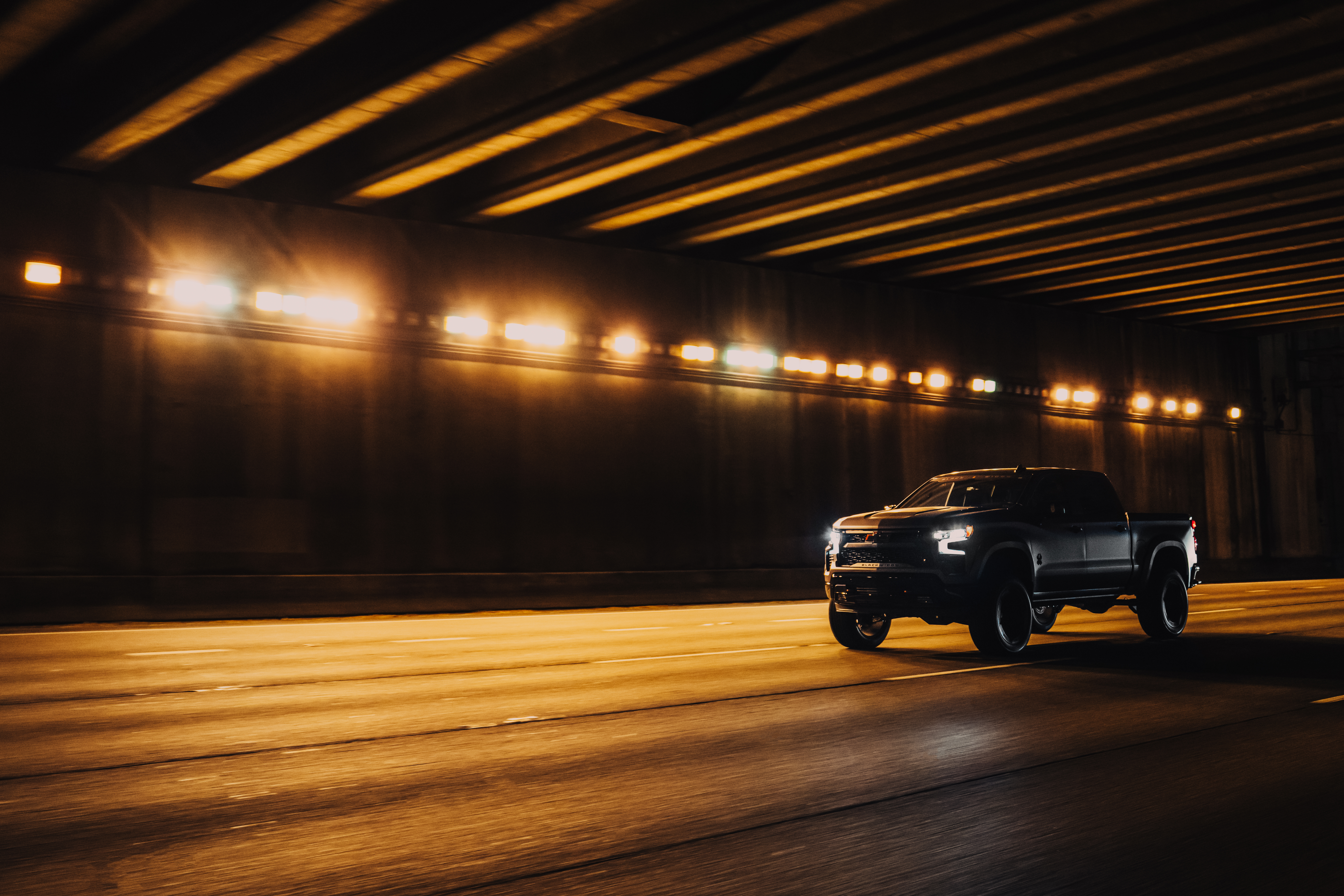 Matte grey lifted truck. Black widow chevrolet silverado 1500 driving under a bridge with bright lights 