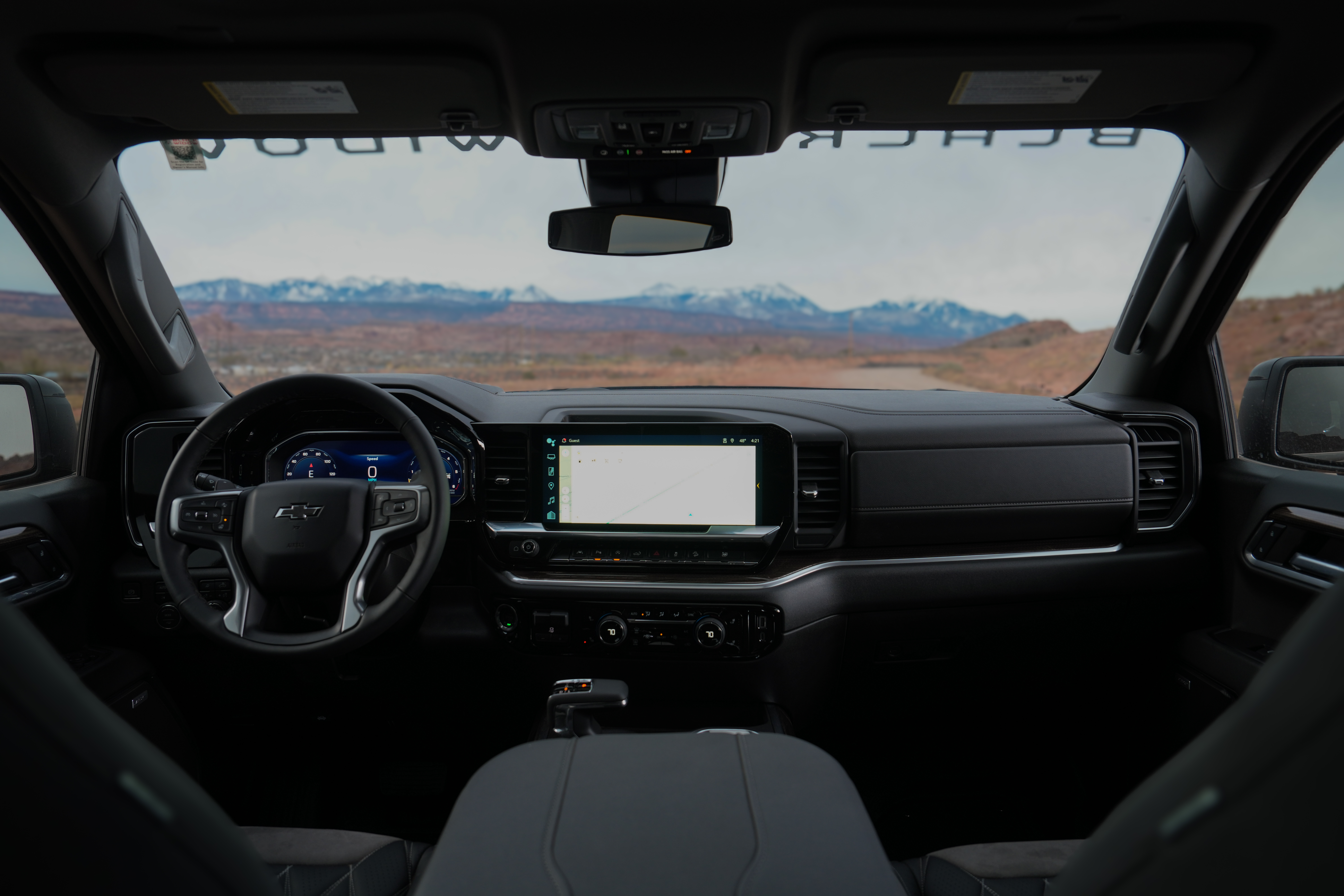 View through the front windoshield of a lifted black widow silverado 1500 out into the moab desert. windshield banner and dashboard technology panels are lit up