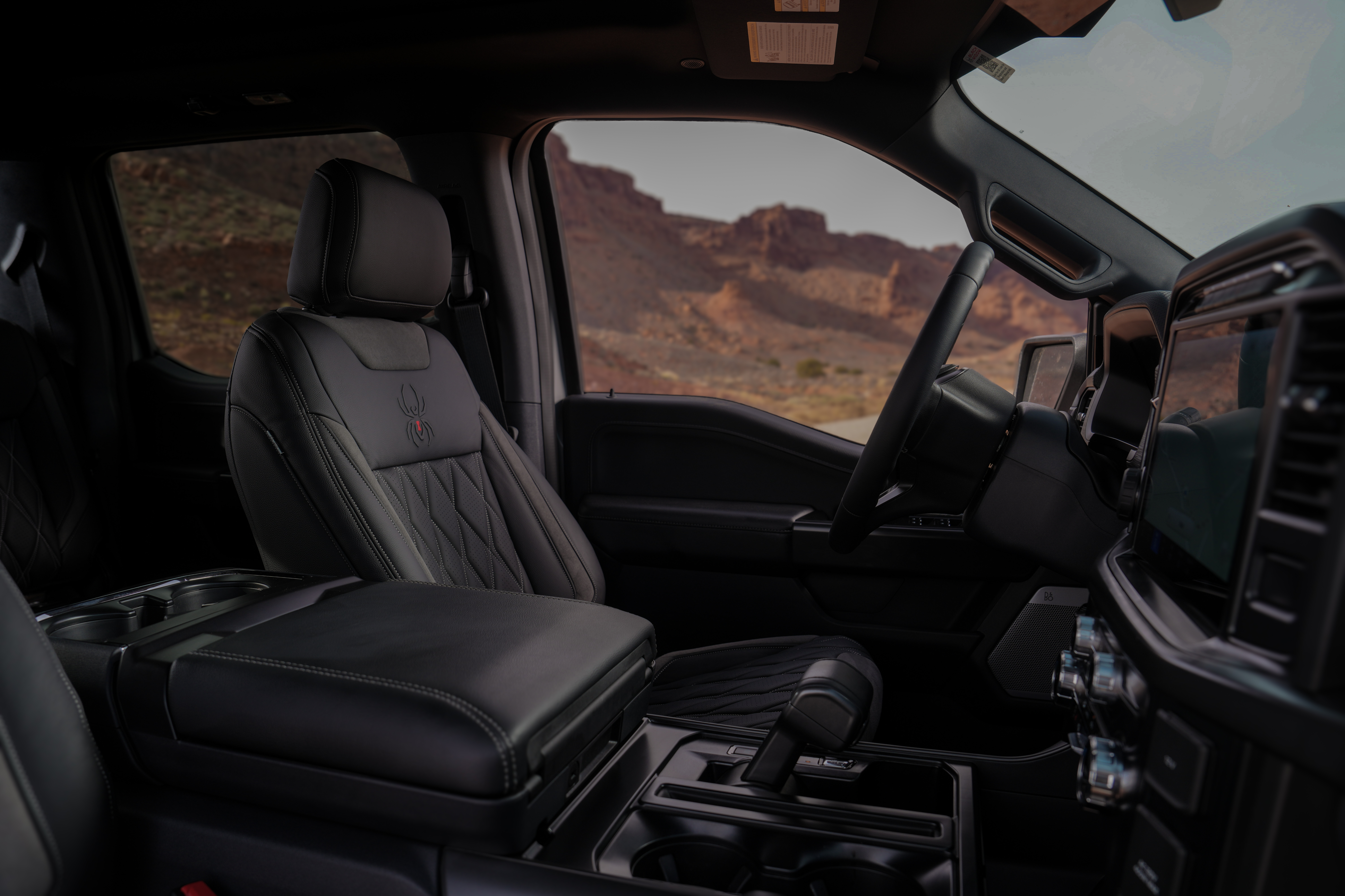 Interior view of a black widow lifted truck with diamond stitched upholstery, black widow spider embossed perforated leather upholstery sitting in moab desert offroad trails