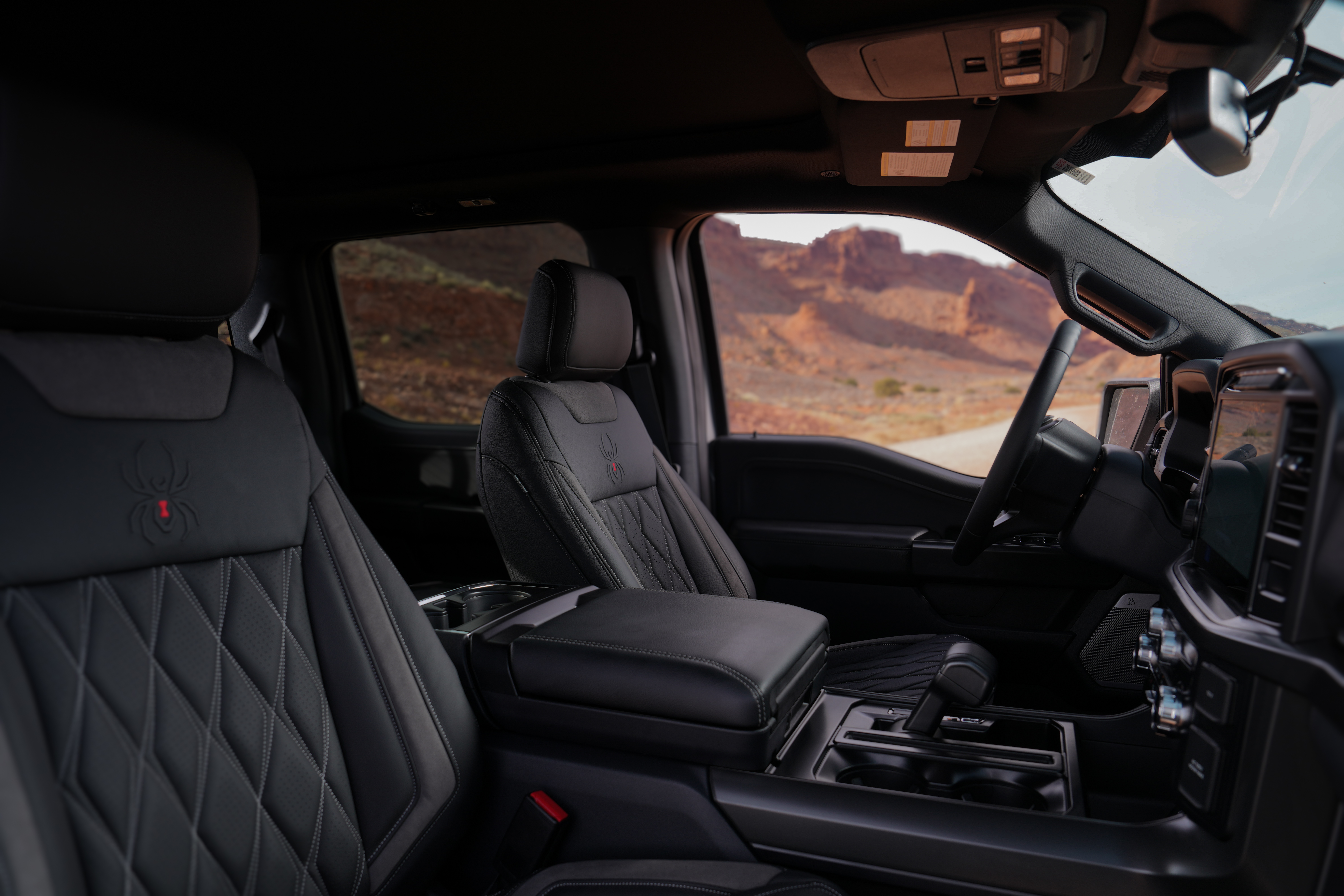 Interior view of a black widow lifted truck with diamond stitched upholstery, black widow spider embossed perforated leather upholstery sitting in moab desert offroad trails