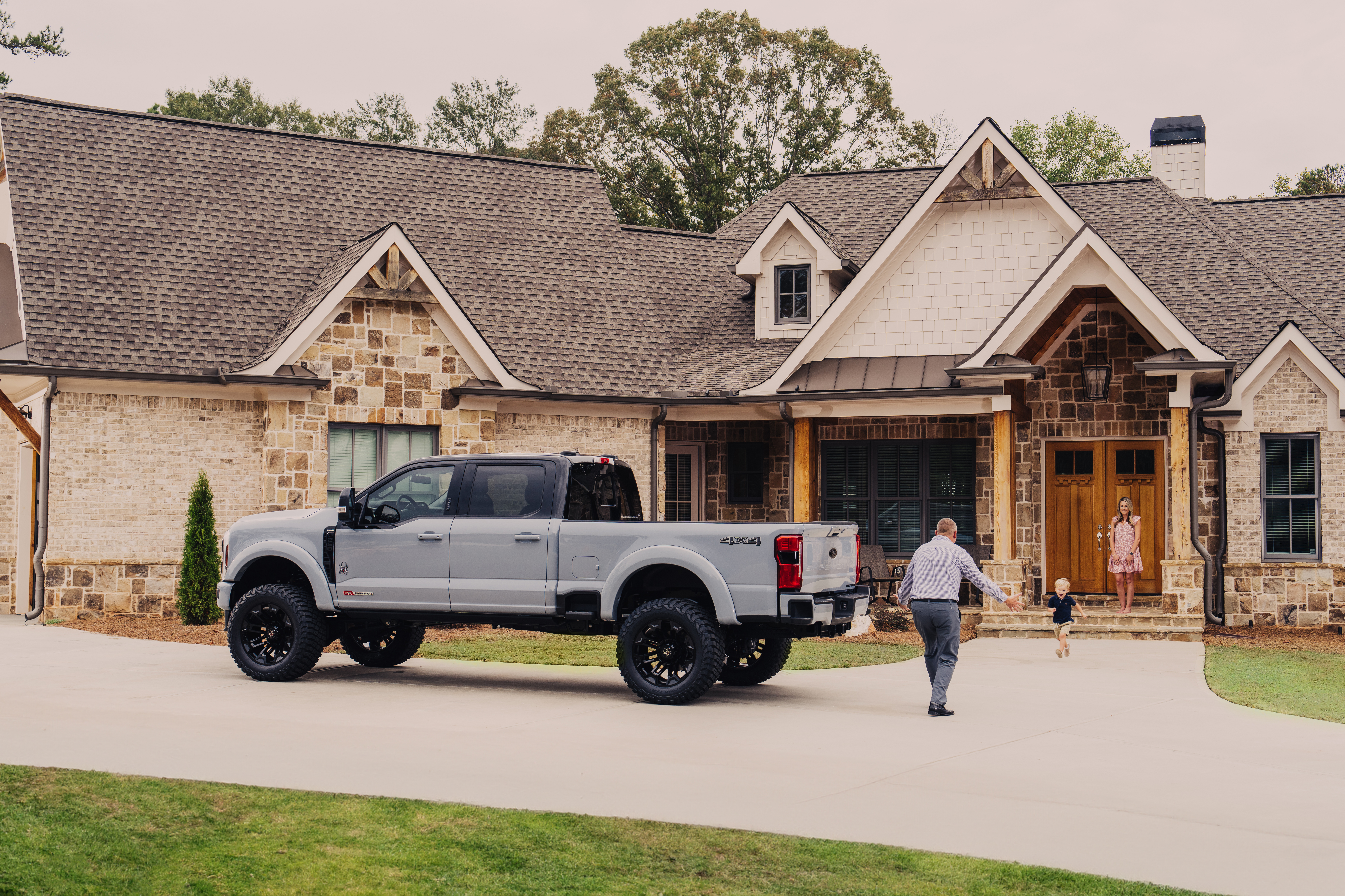 Grey and black hi-hat paint on a ford superduty parked outside of a beautiful large home with a man being greated by his two kids with arms out stretched and wife standing on front steps