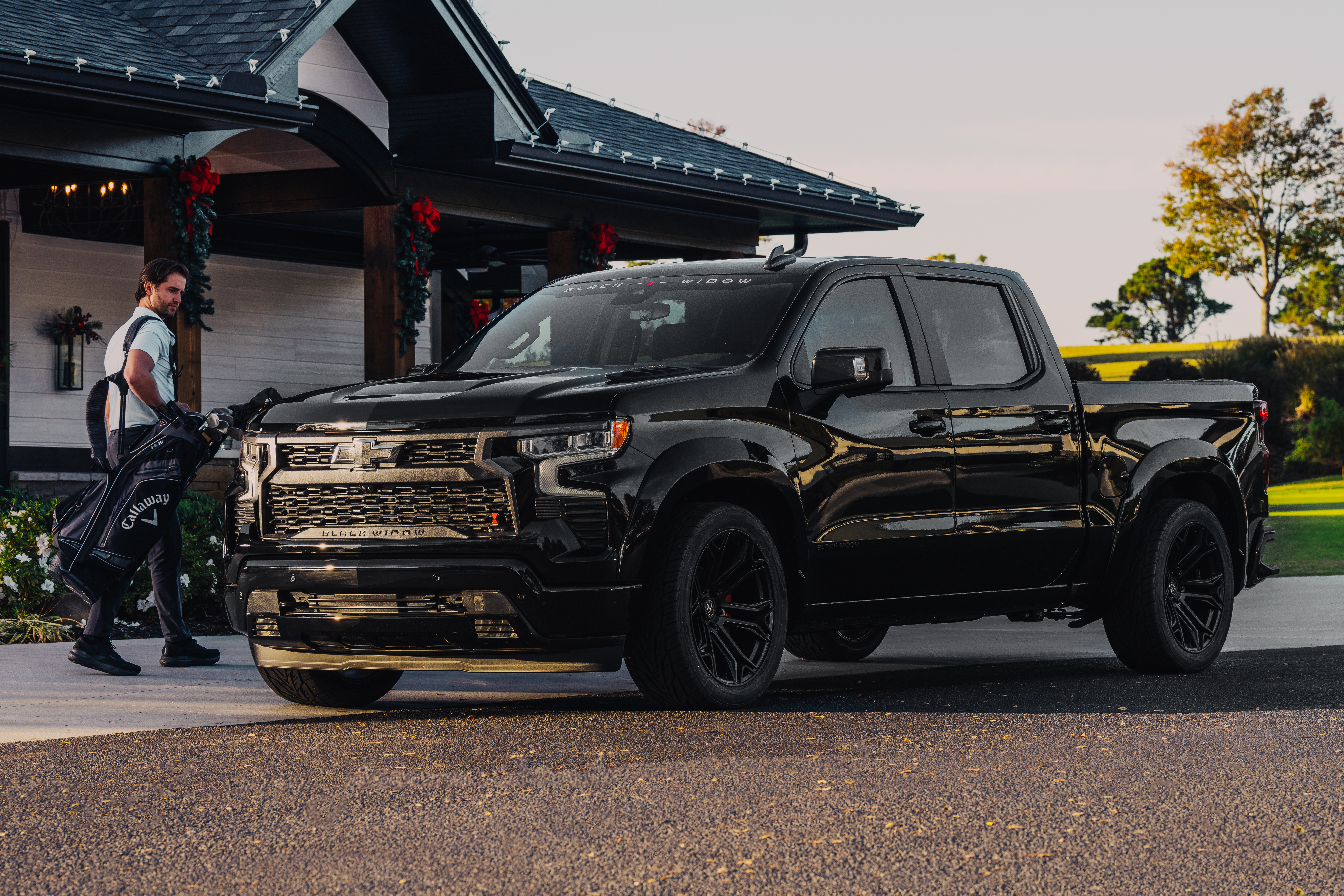 Black chevrolet silverado 1500 lowered black widow sr truck with custom grille and black wheels parked outside of a golf pro shop with golfers holding golf bags