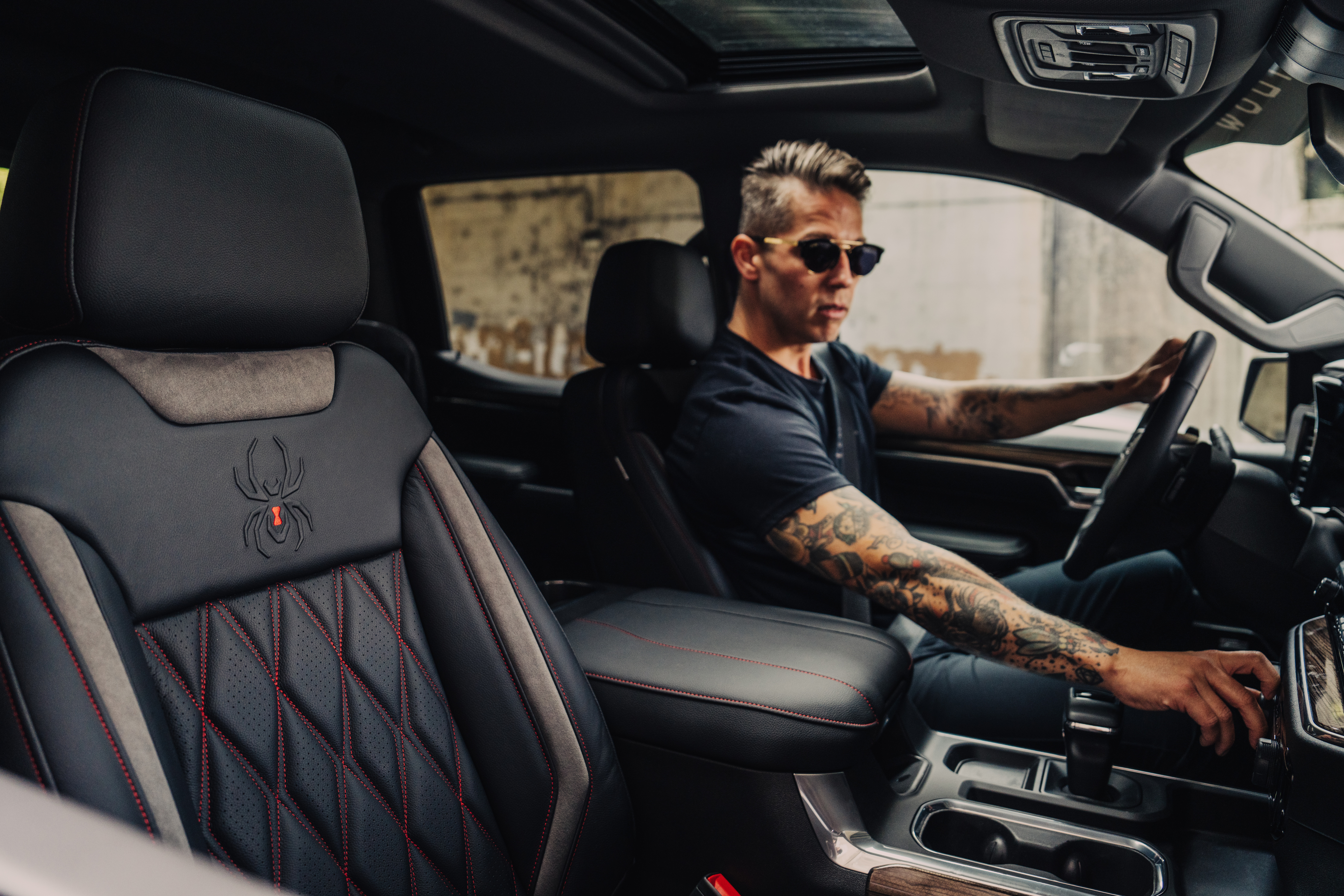 man with tattoos sitting in the driver's seat of a black widow lifted truck