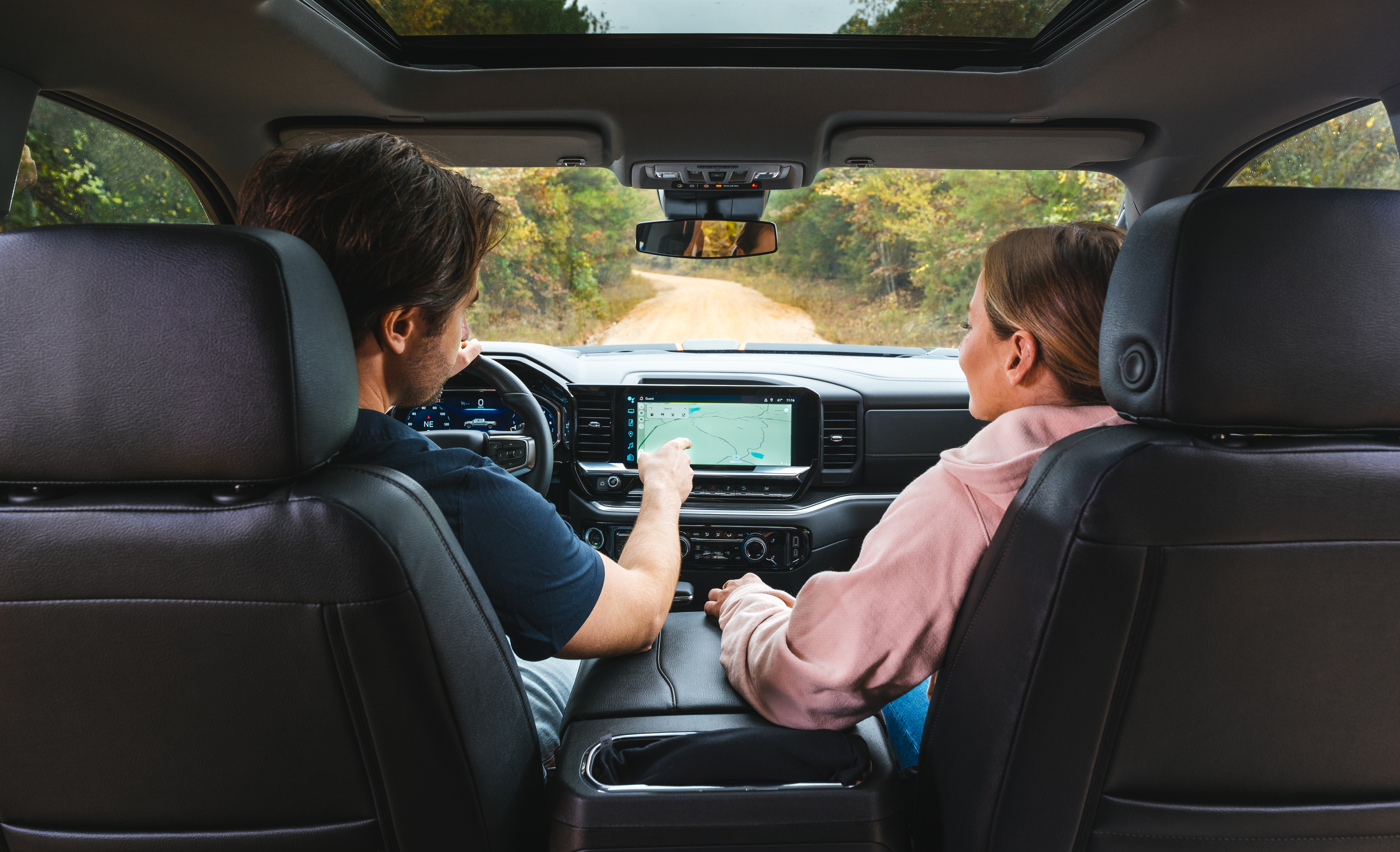 a couple sitting in the front seat of a lifted black widow chevrolet silverado 1500 truck. man is pointing out the map on the dashboard touch screen