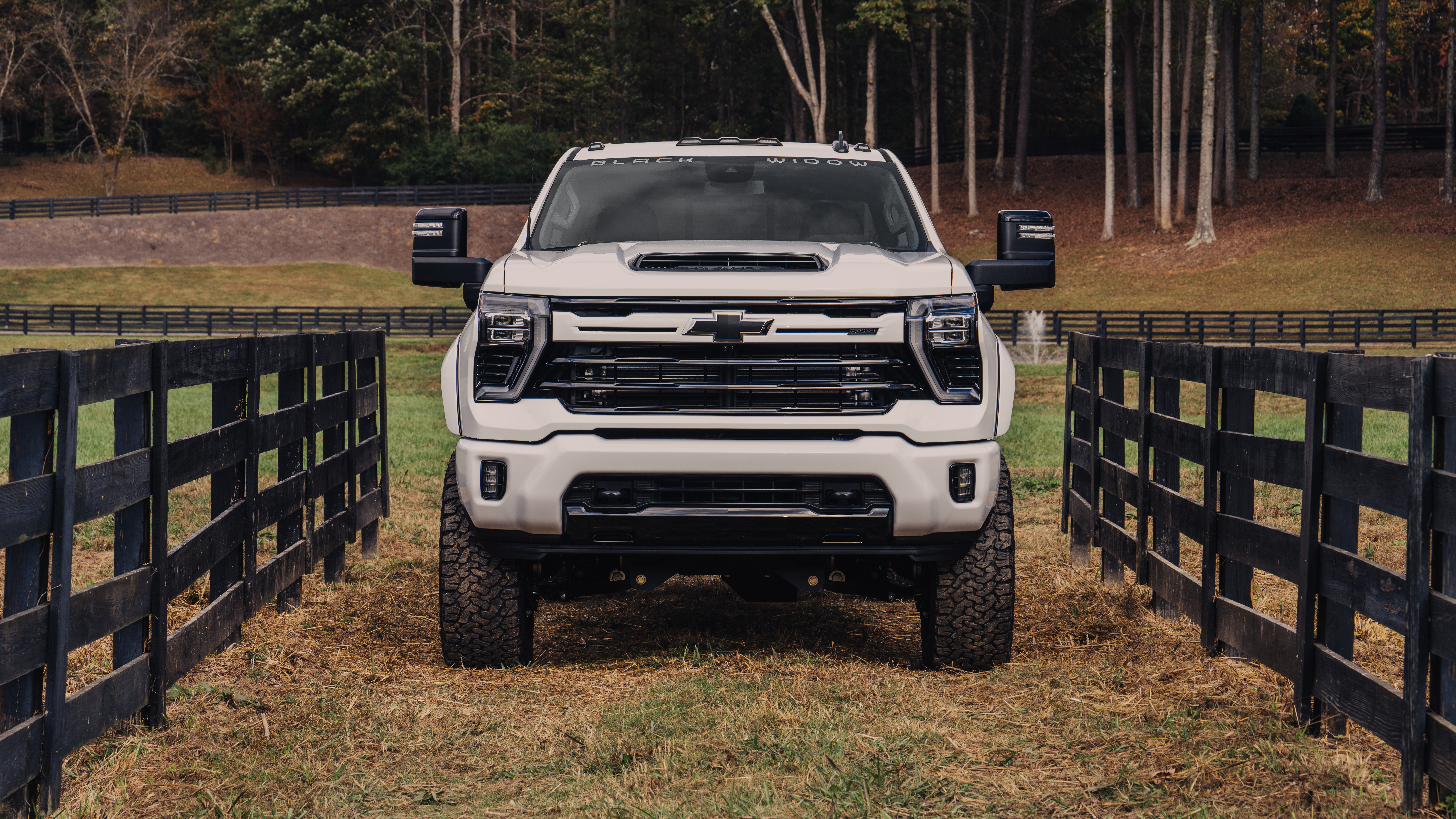 White chevrolet silverado hd black widow lifted truck parked on a horse farm with stable fencing