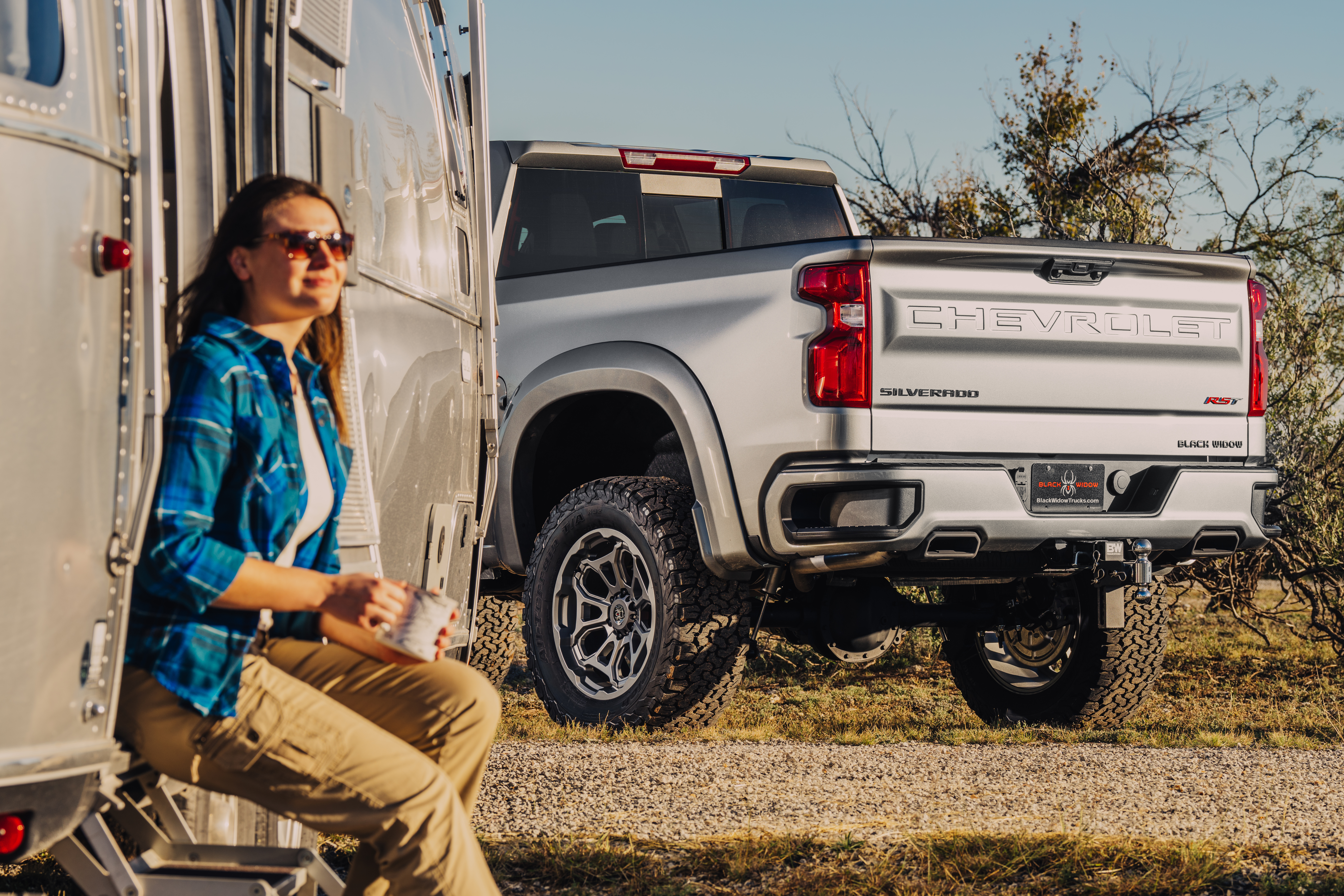 Woman sitting at air stream camp site with matte silver chevrolet silverado hd 2500 