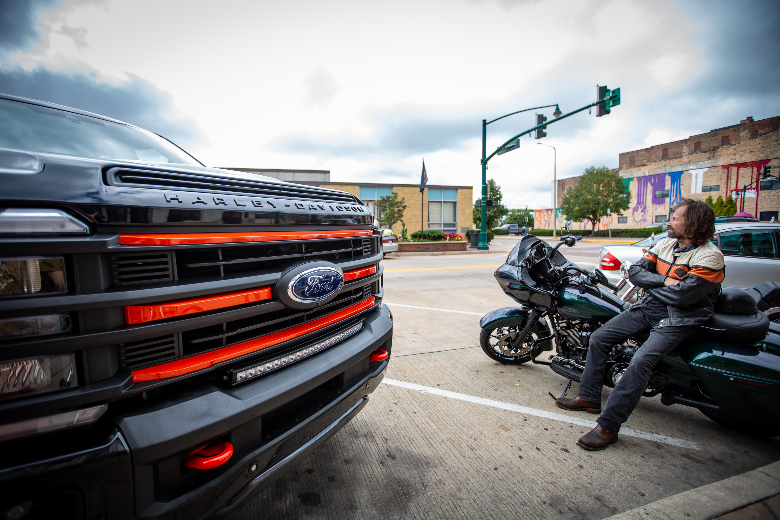 harley davidson truck parked next to a biker leaning on a harley-davidson motorcycle wearing a Harley davidson jacket