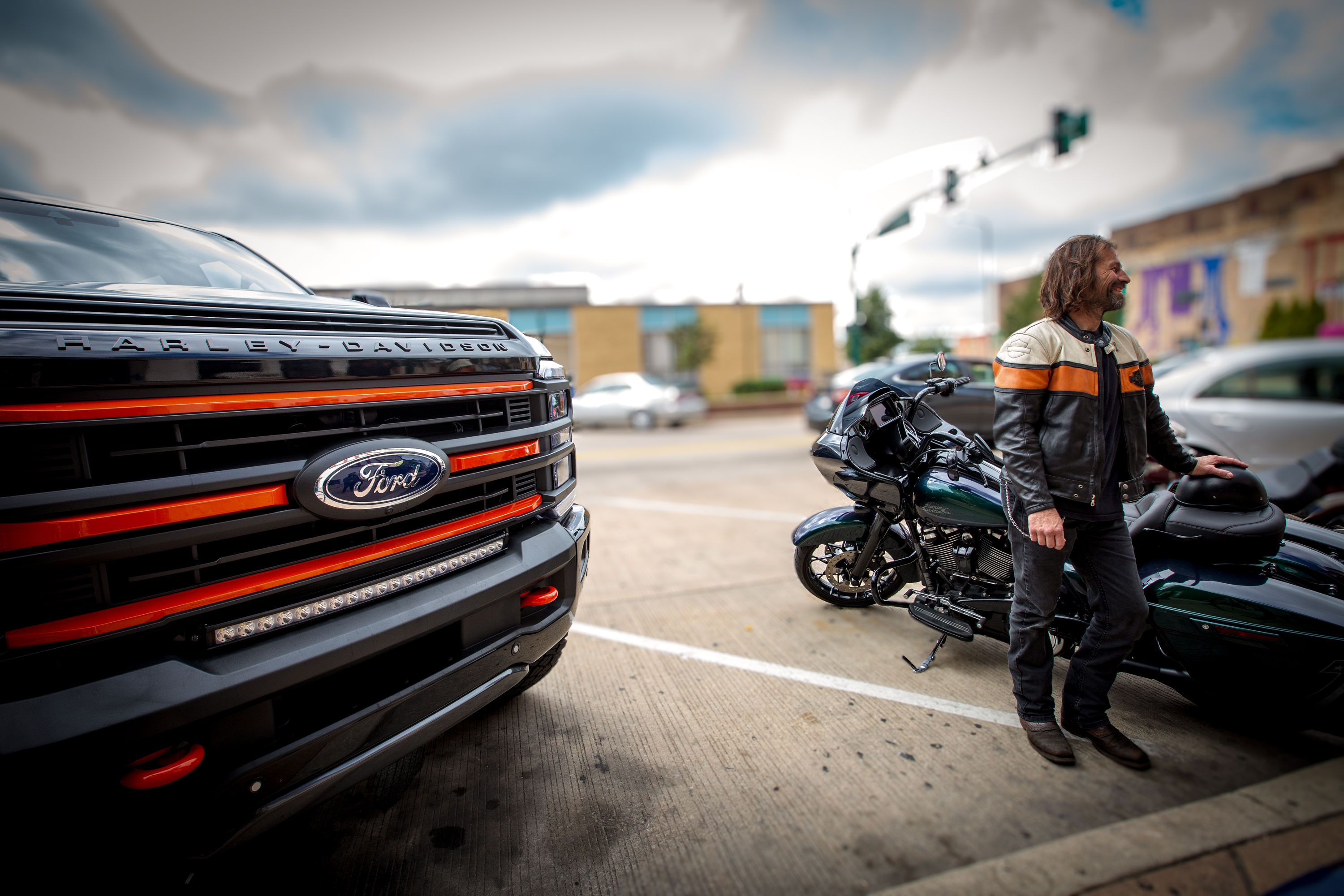 HARLEY DAVIDSON SUPER DUTY LIFTED TRUCK WITH A MAN IN A MOTOCYCLE JACKET AND HIS HARLEY BIKE