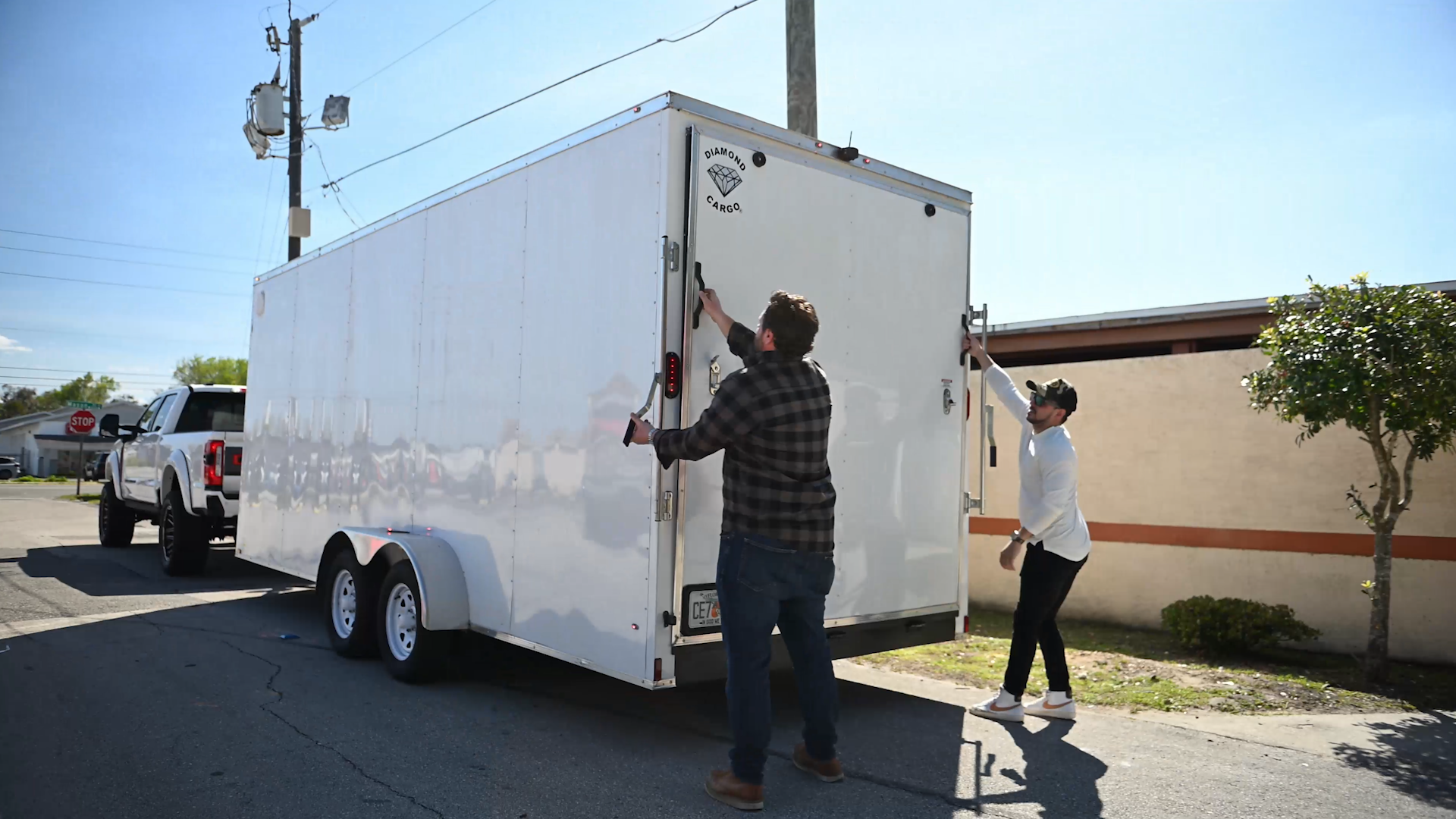 two guys opening a covered trailer thats being towed by white lifted ford superduty Harley-Davidson truck