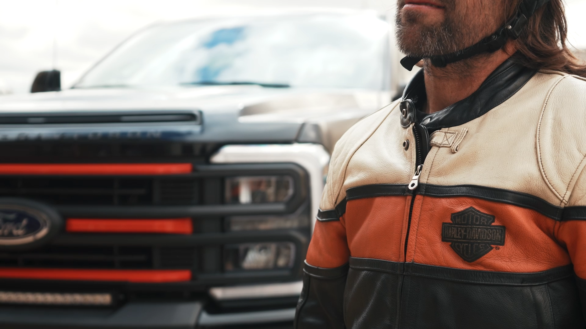 man wearing Harley-Davidson motorcycle jacket next to a black ford superduty lifted Harley-Davidson truck