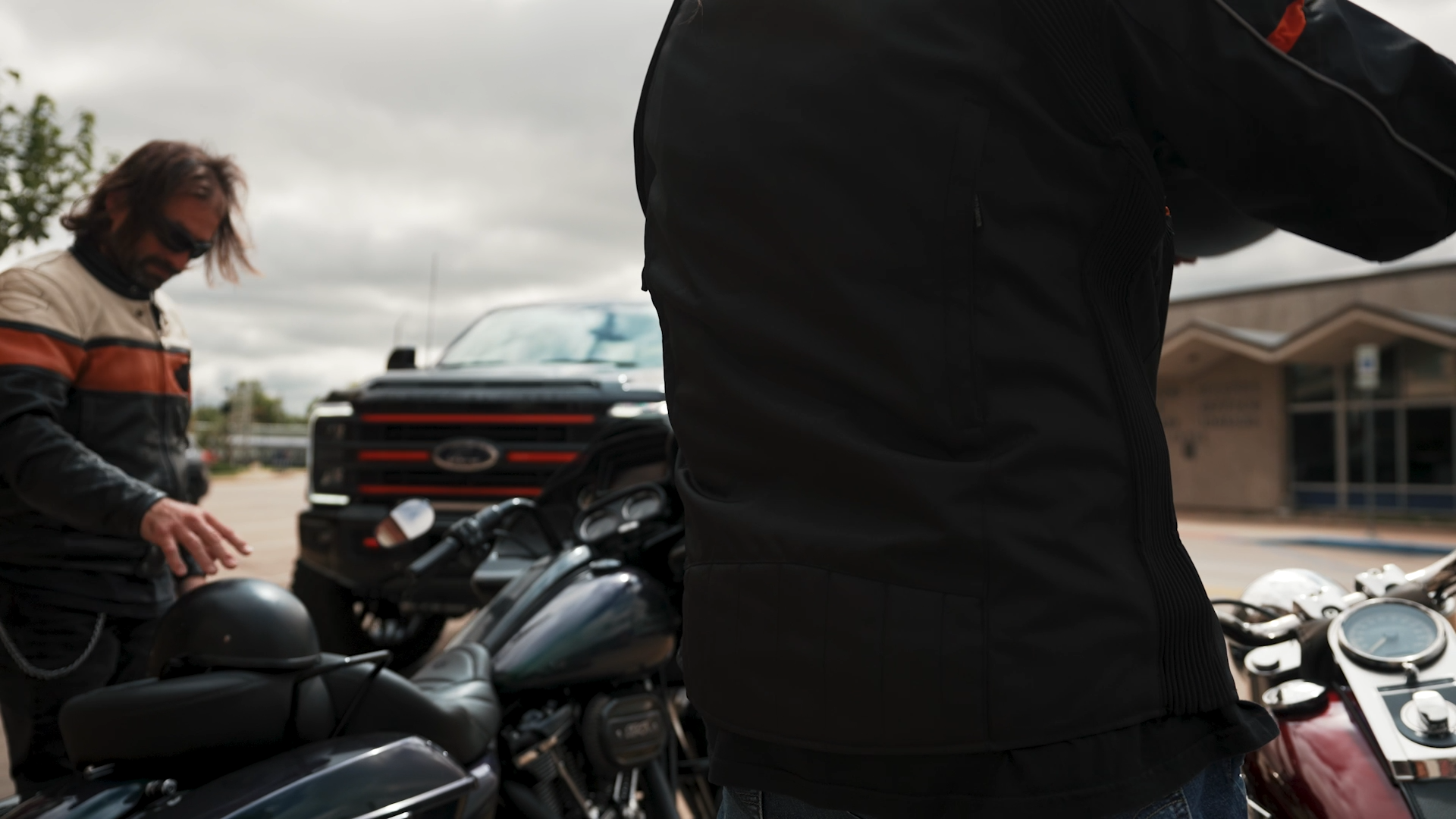two motorcyclists stepping off their bikes in front of a black superduty lifted Harley-Davidson truck