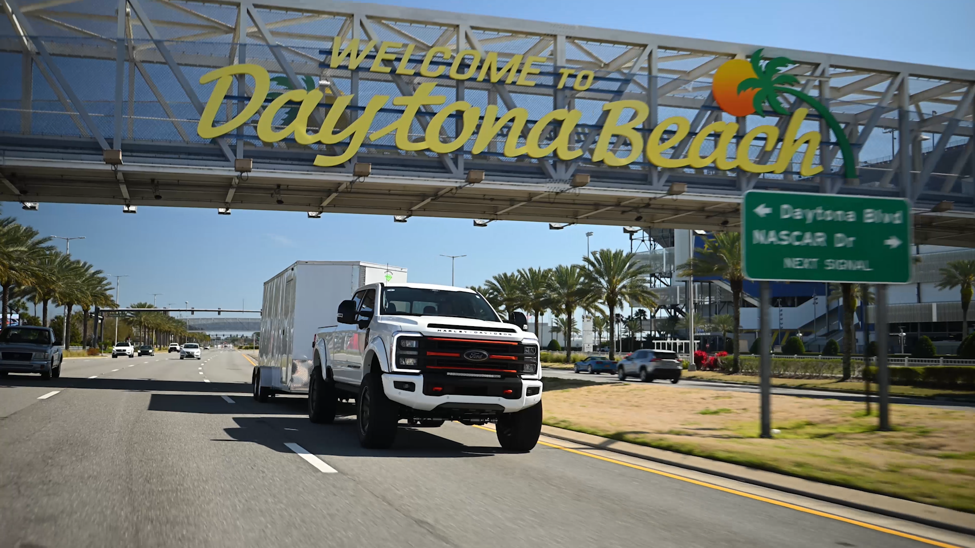 white ford superduty Harley-Davidson lifted truck towing a covered trailer under the daytona beach sign