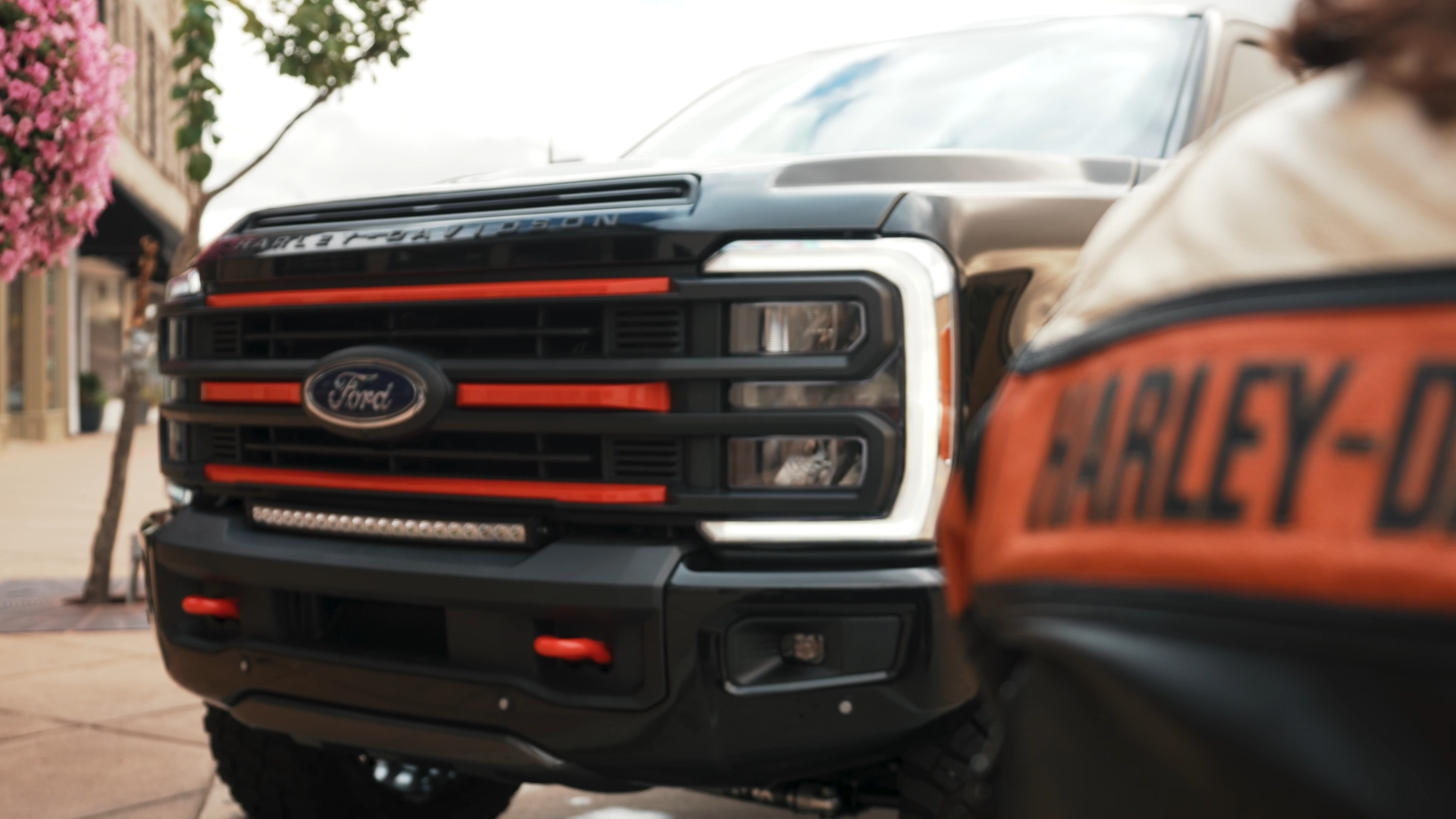 Harley-Davidson black ford superduty lifted truck next to man wearing Harley-Davidson motorcycle jacket