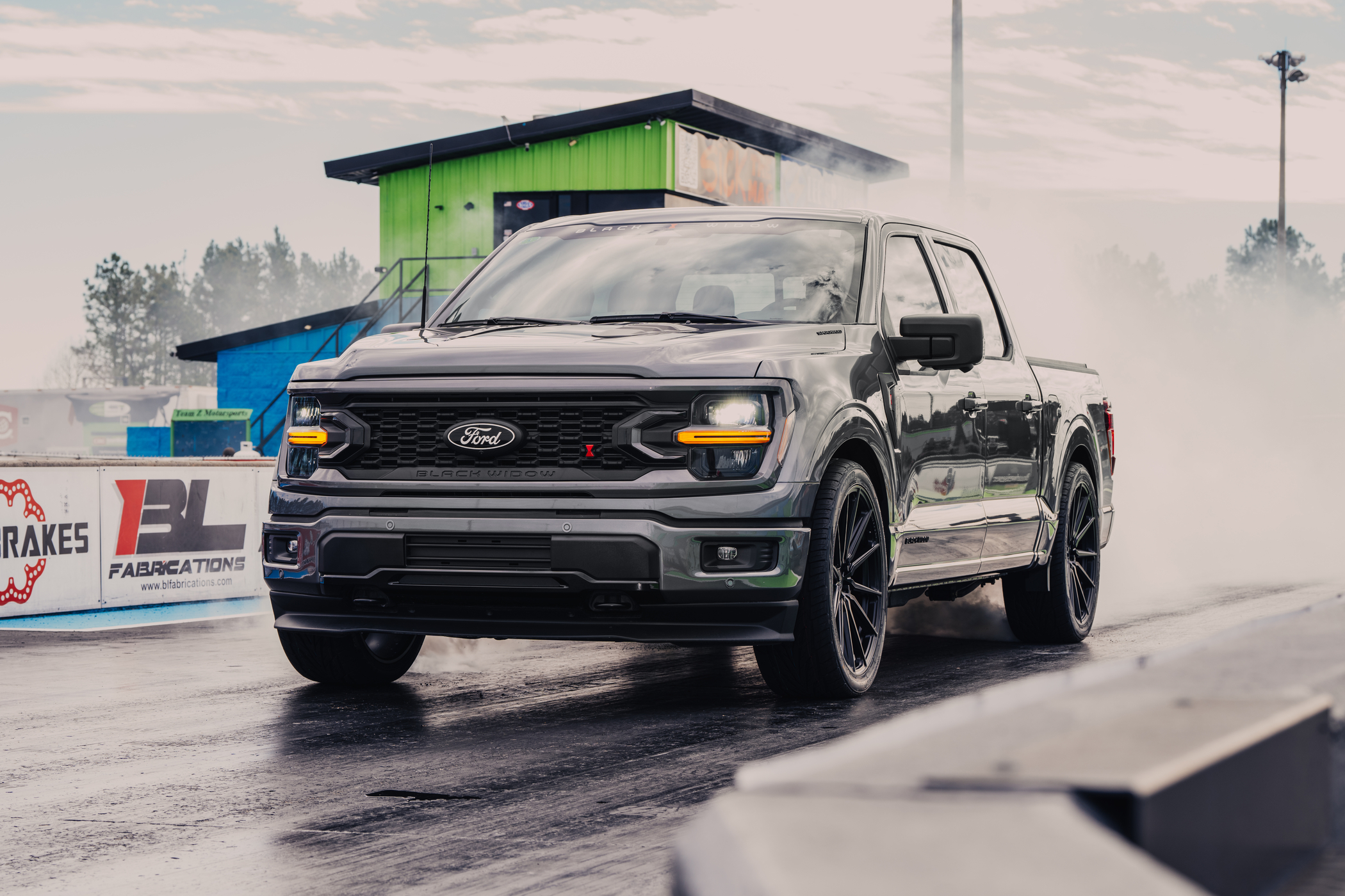 Lowered Black Widow F-150 truck at the drag strip pulling off the line doing a burnout with smoke billowing.