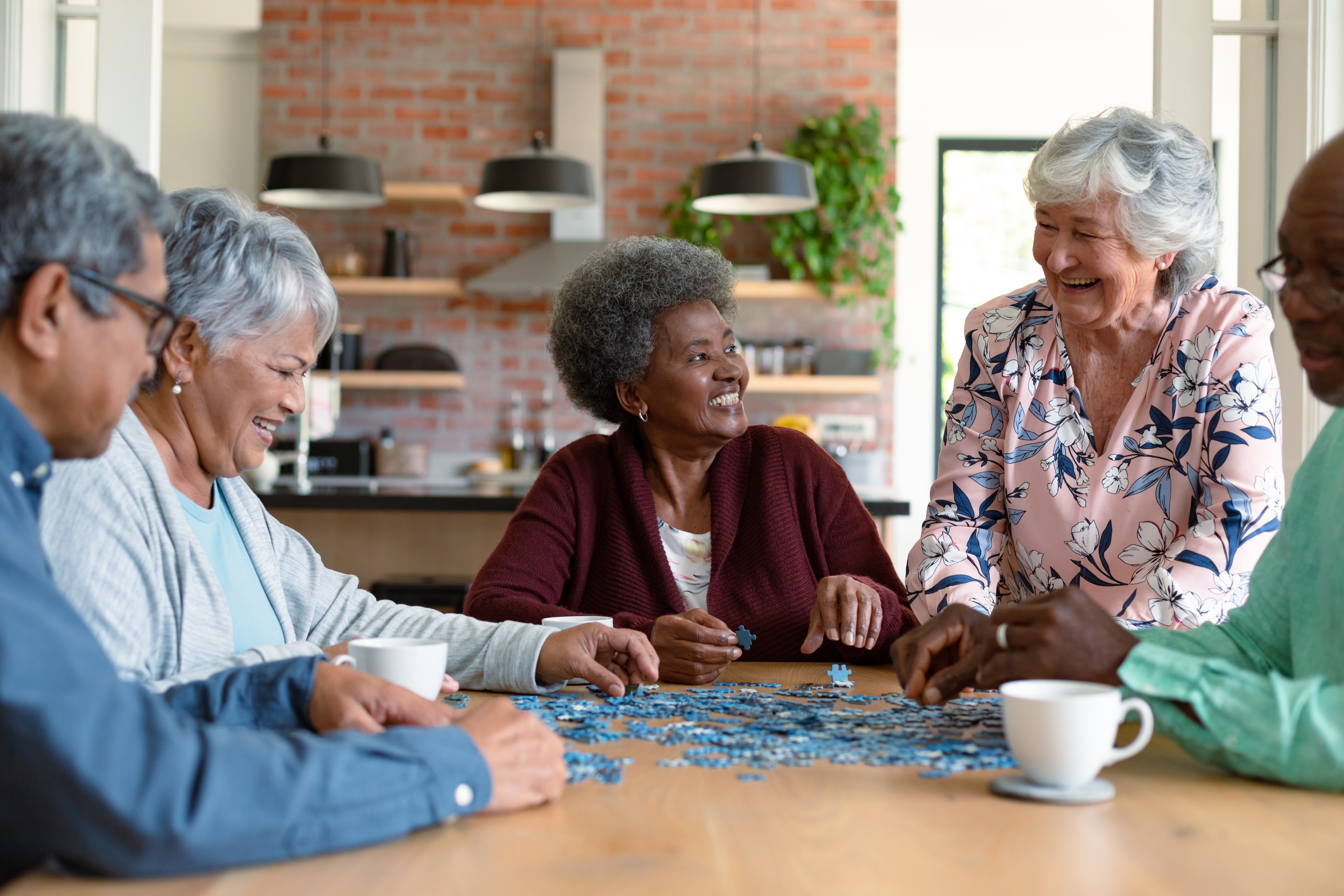 Group of older adults drinking coffee, talking, and working on a puzzle together.