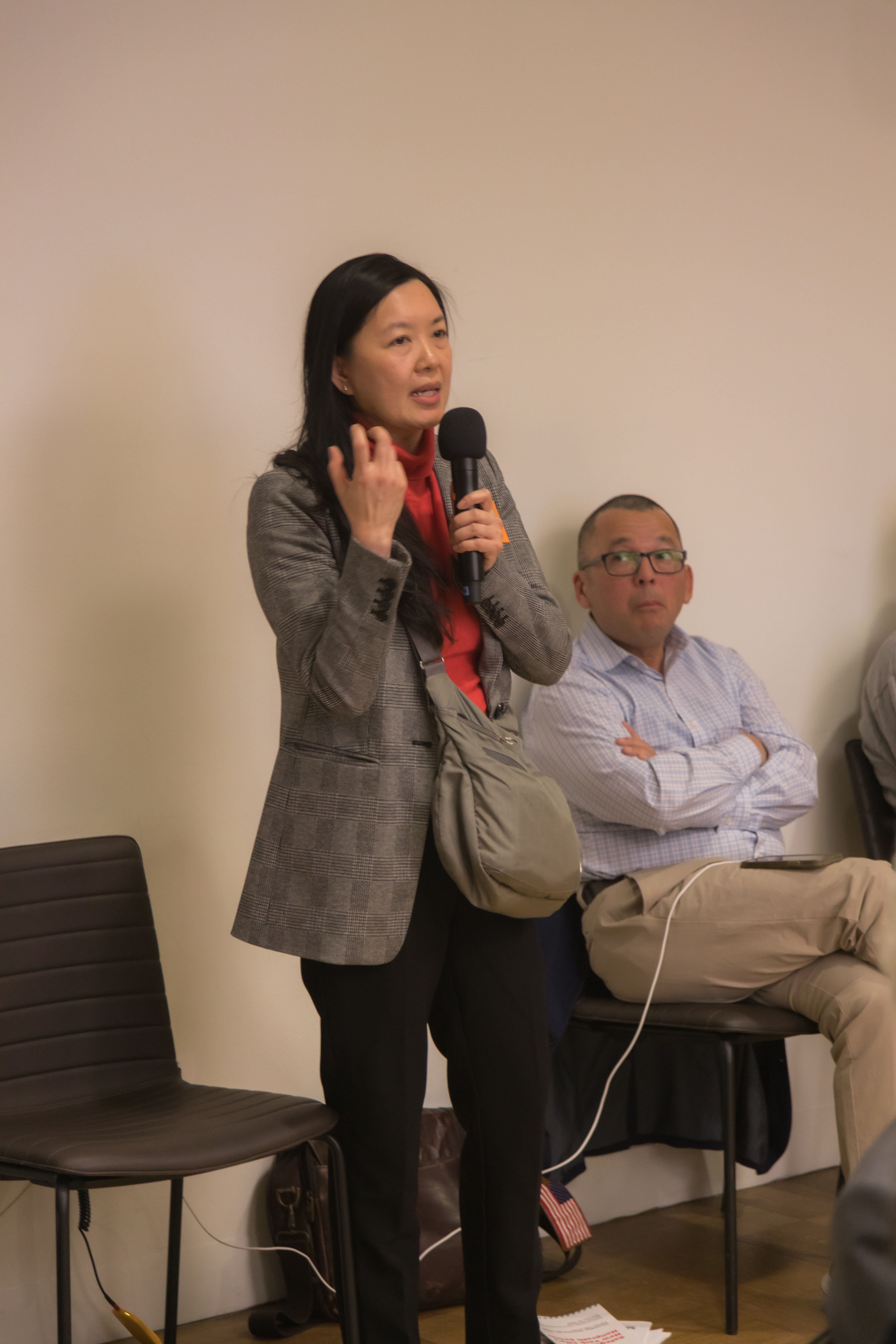 A woman in a plaid blazer speaks into a microphone at a Nonprofit New York convening as attendees listen.