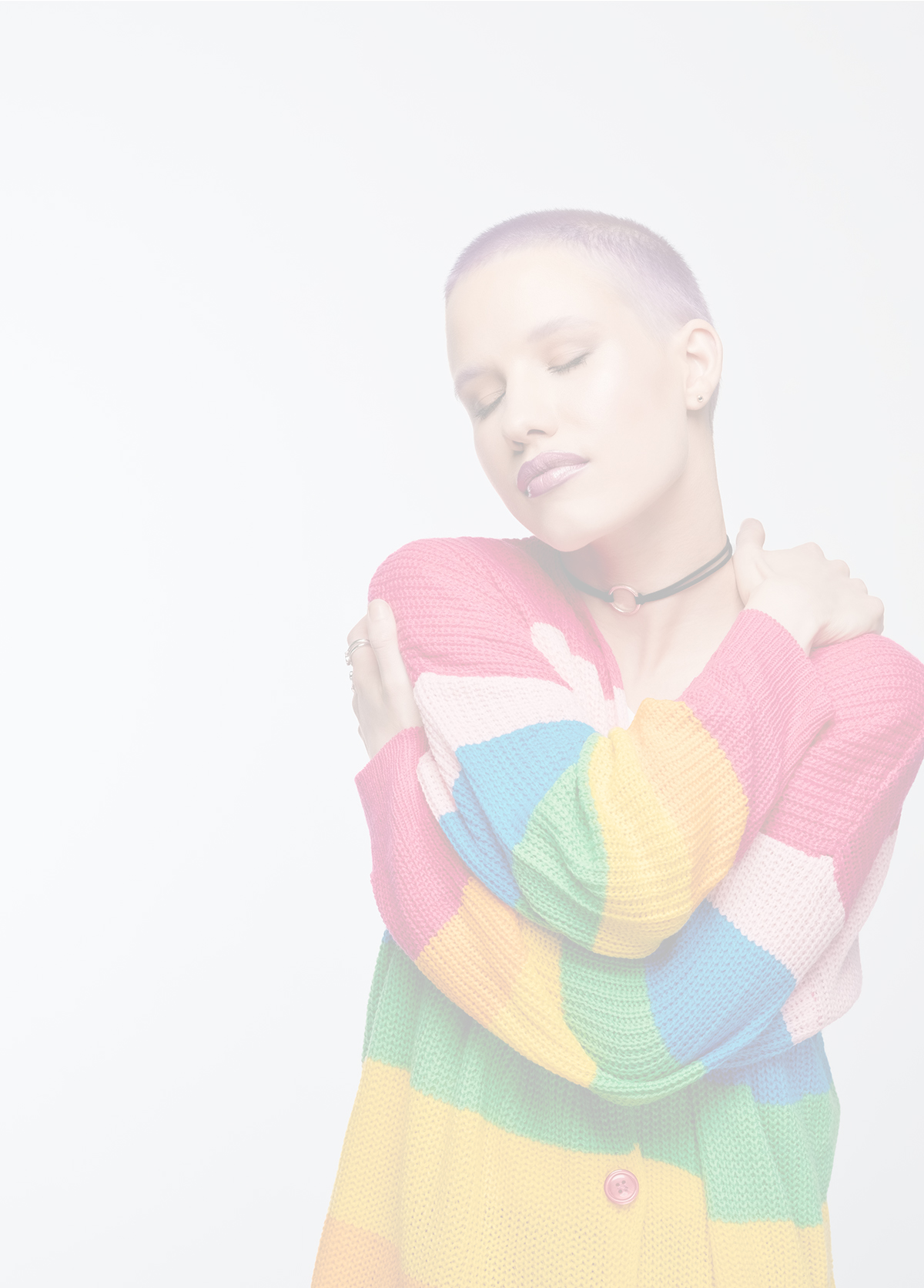 Young woman wearing rainbow cardigan hugging self. Studio portrait on white background.