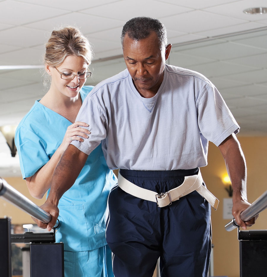 A female physical therapist assists an older male patient while doing gait training.