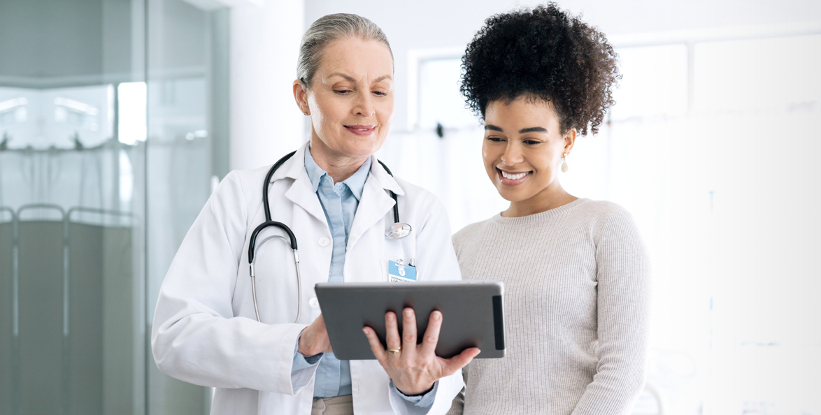Doctor in white lab coat holding a tablet in front of a smiling patient.