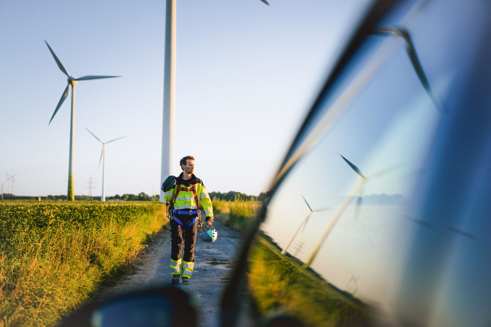 a worker in a high visibility vest walks in front of a tall windmill