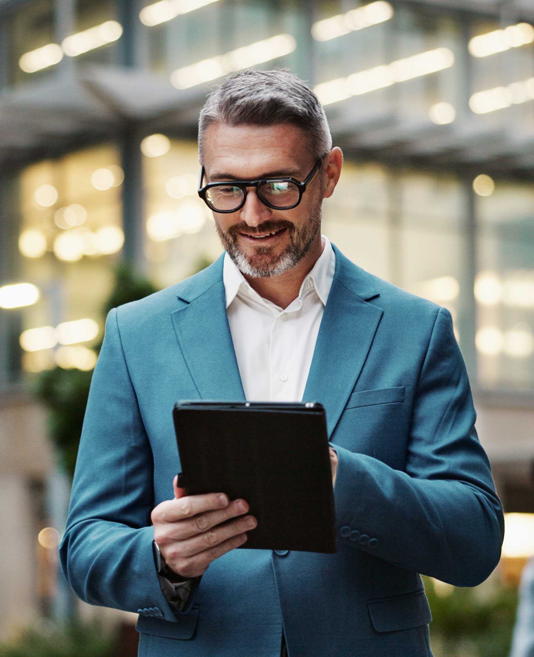 Smiling businessman on tablet in front of building