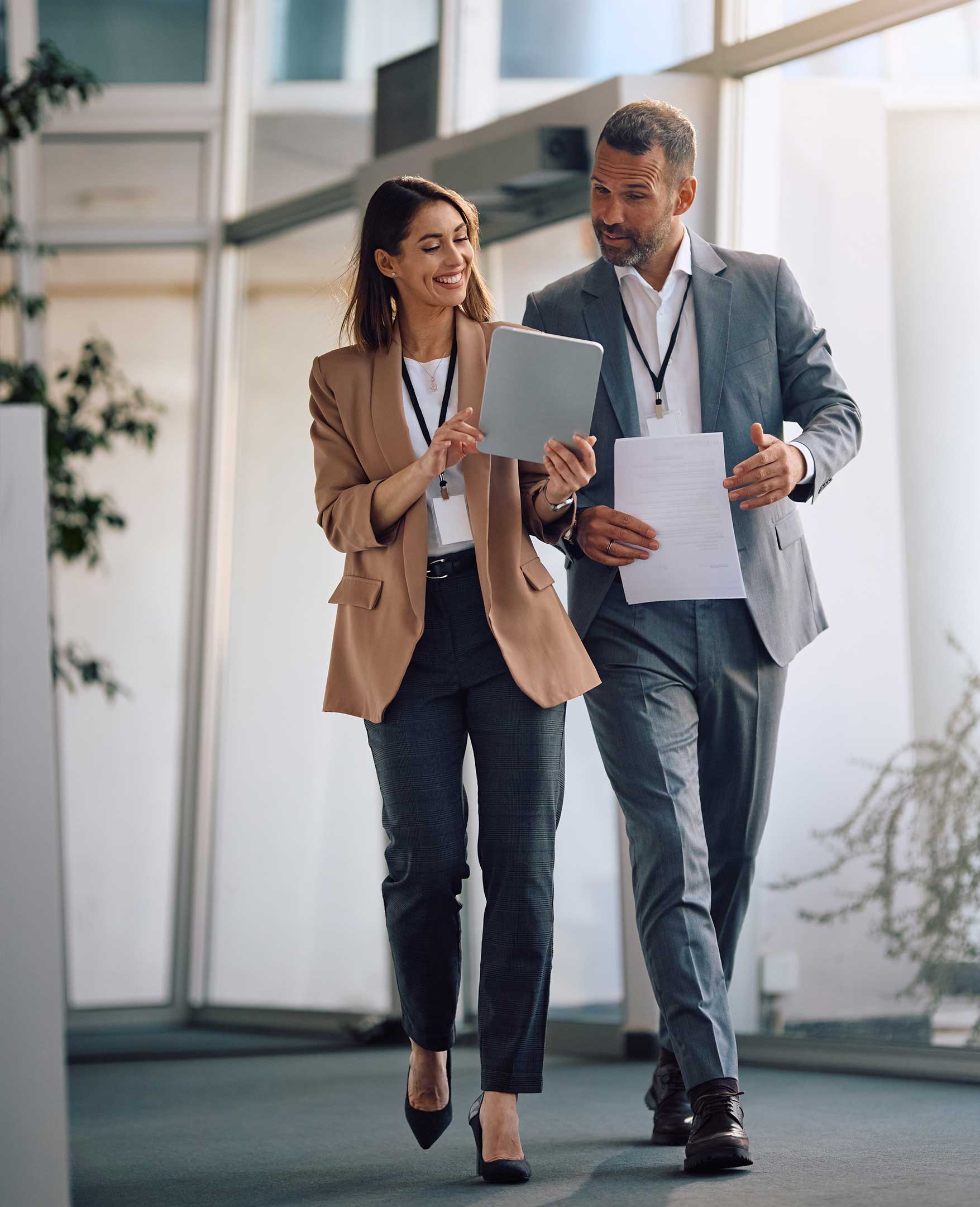 Two smiling office workers walking through an office and looking at a tablet