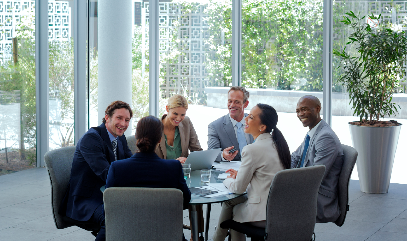 6 businesspeople in an enterprise building around a table in front of greenery.