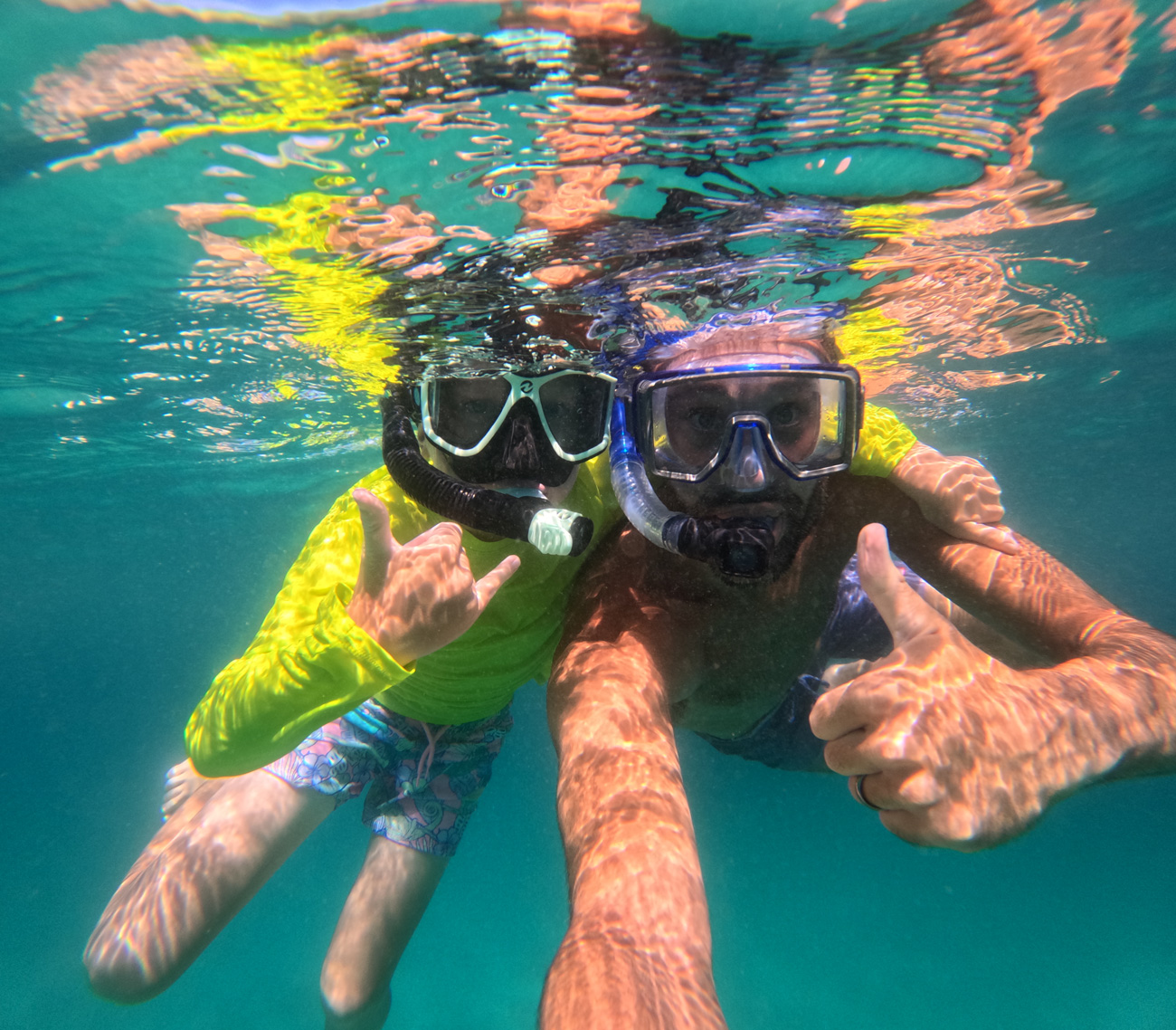 Two teenagers are wearing scuba goggles and taking a selfie underwater.