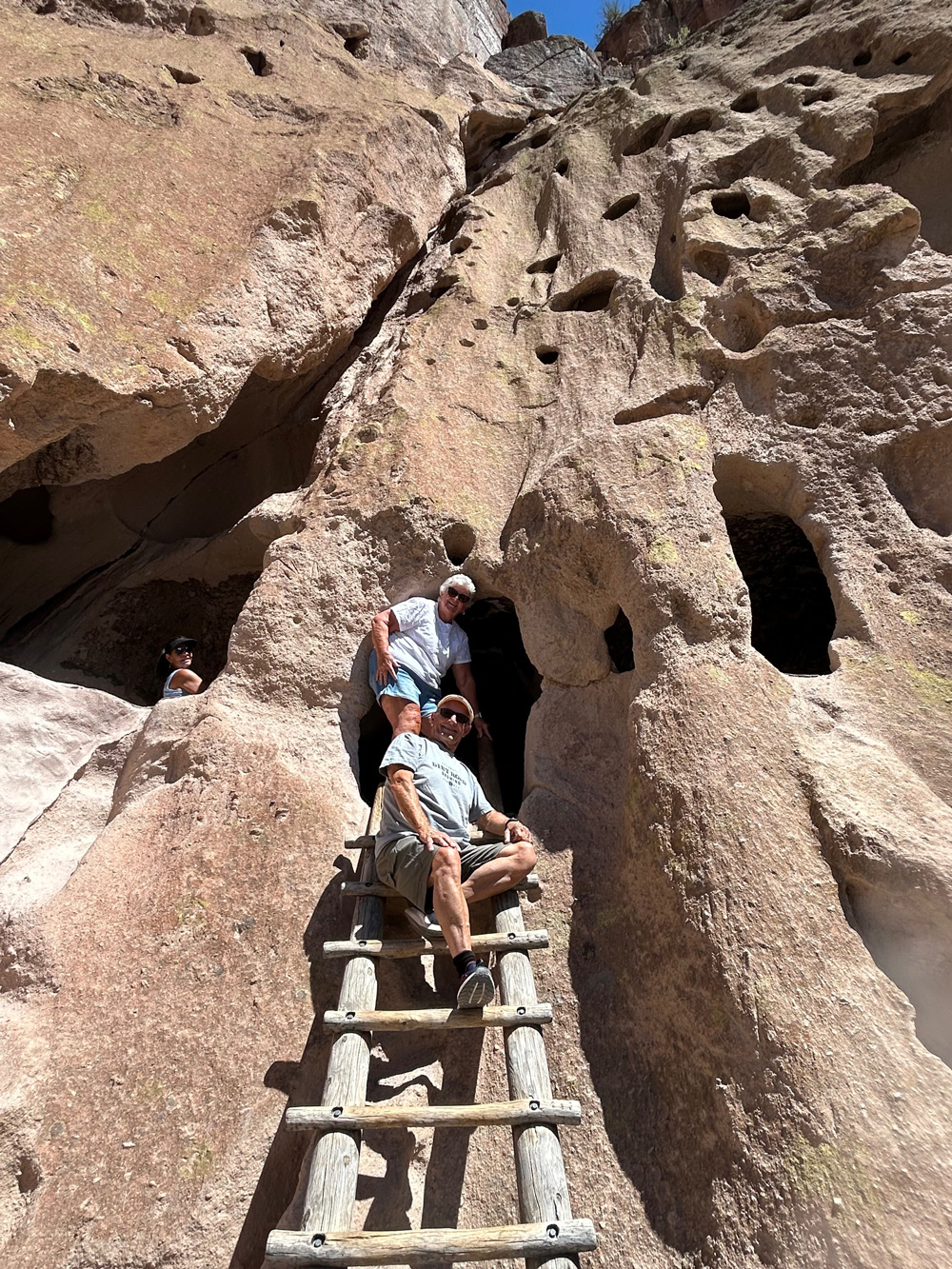 A couple in their 60s are resting on the edge of a cave, smiling down at the camera.