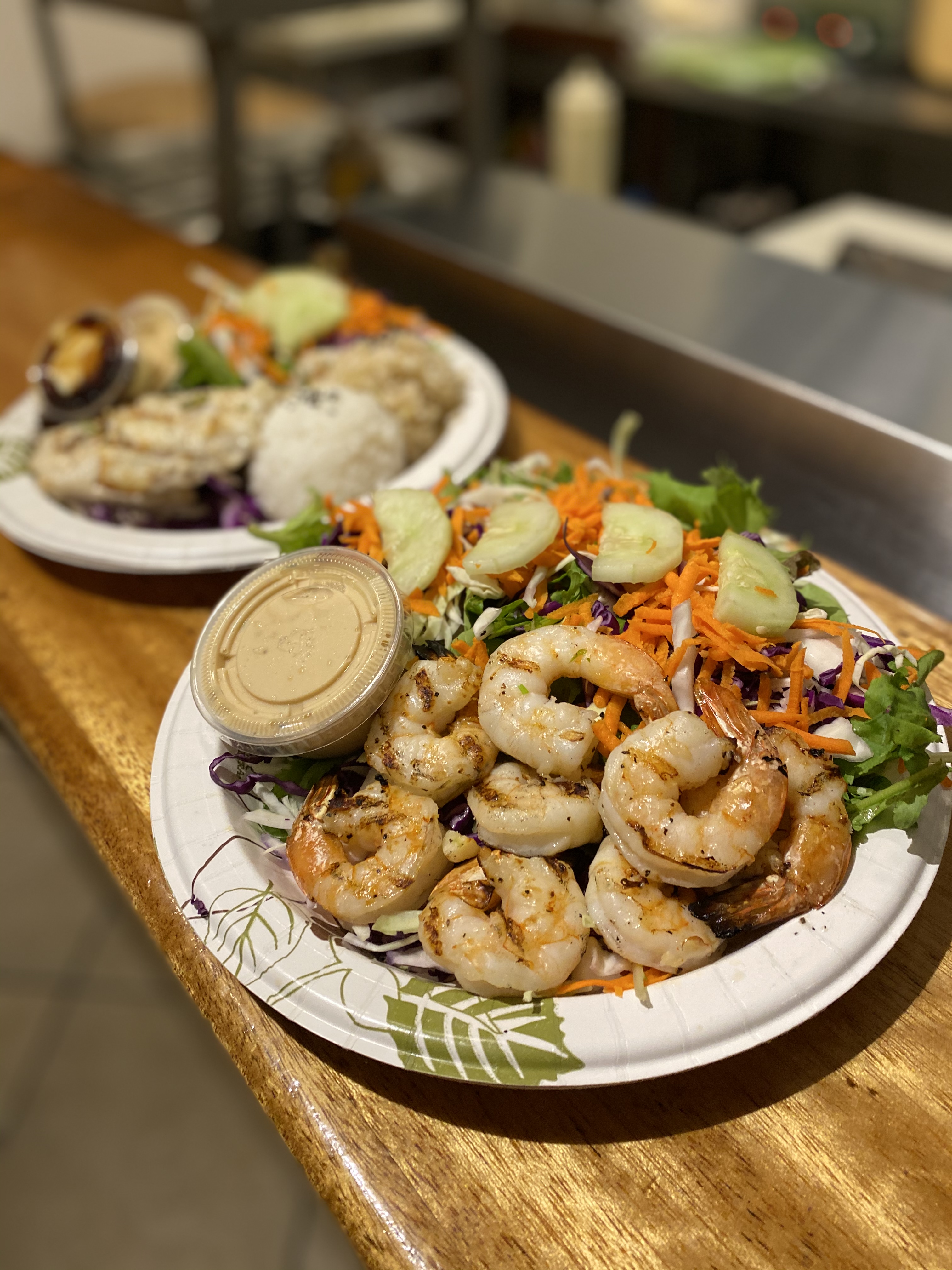 Paper plate filled with shrimp, salad, and a side of dipping sauce