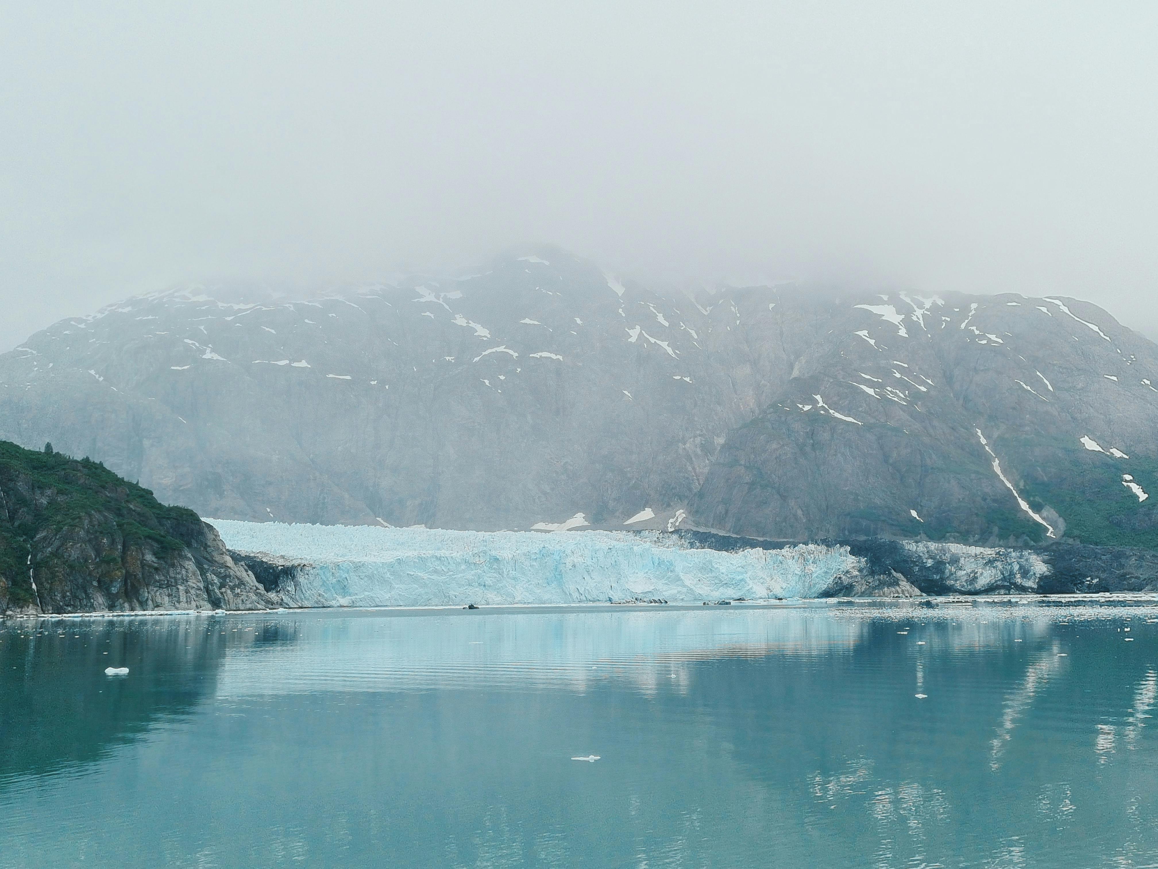 Foggy view of a mountain with a bright blue glacier along edge of the water
