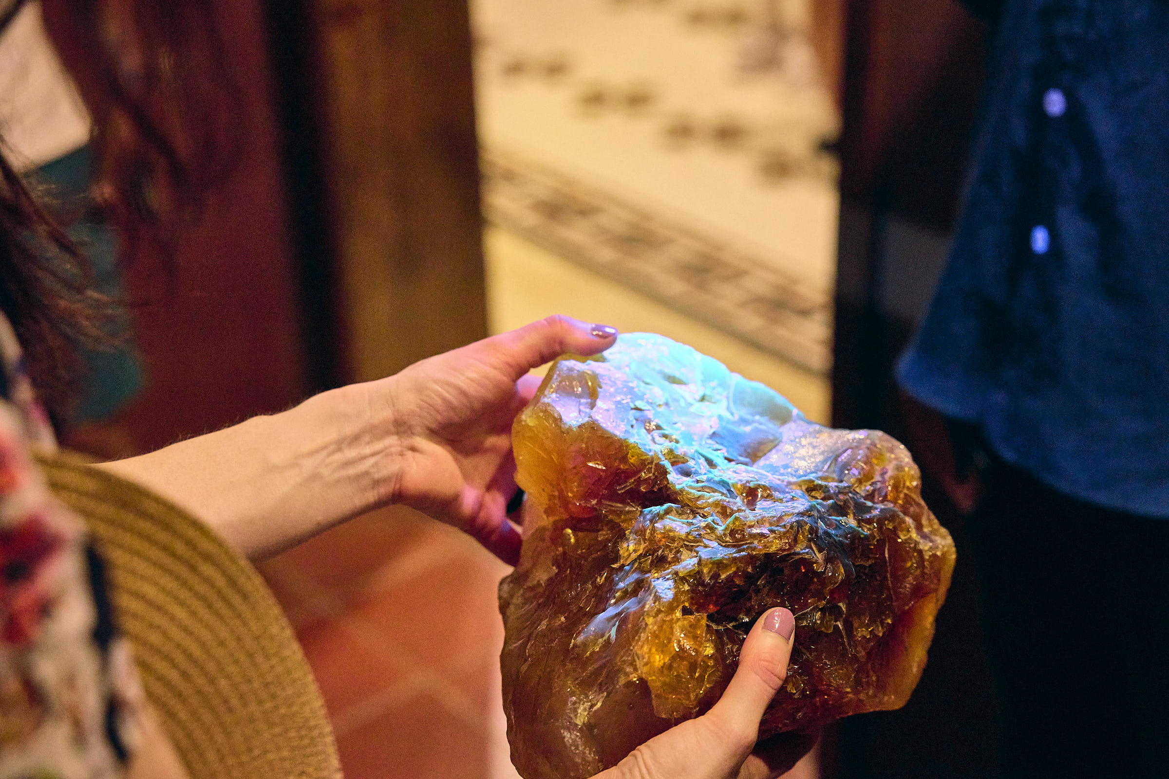 Hands holding a large chunk of amber, a brownish gemstone that glows blue when light shines on it