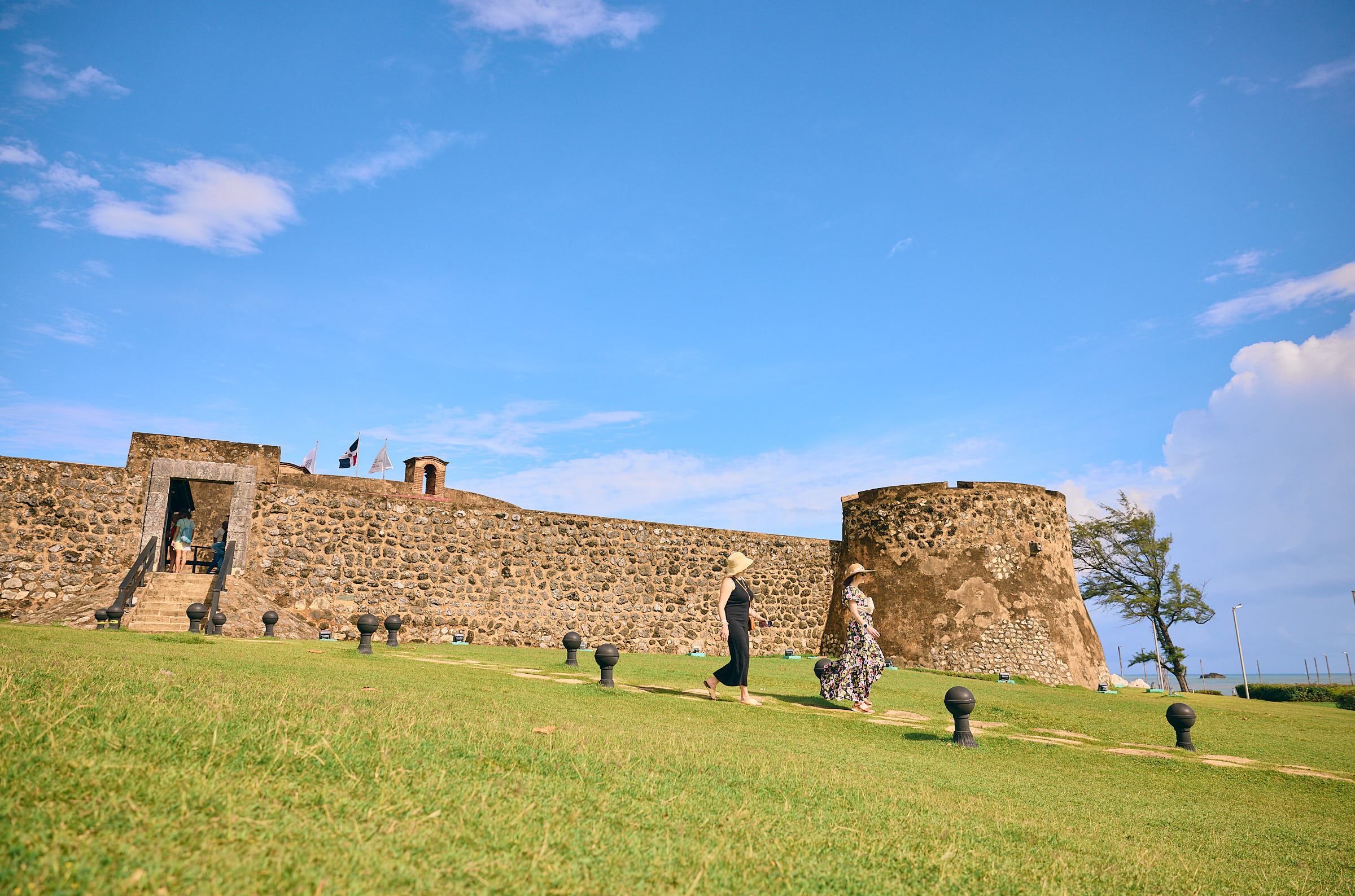 Two people walking down a hill with a rustic stone fort behind them