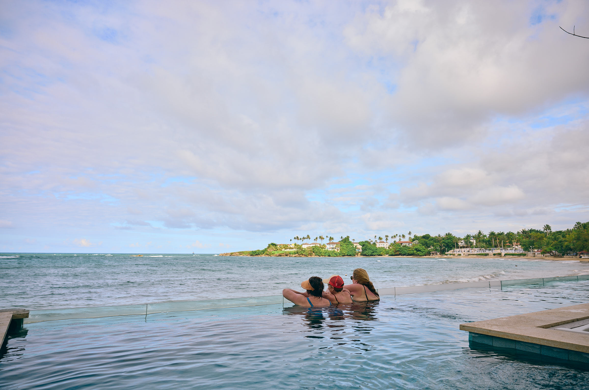 Three women resting at the edge of an infinity swimming pool by the ocean