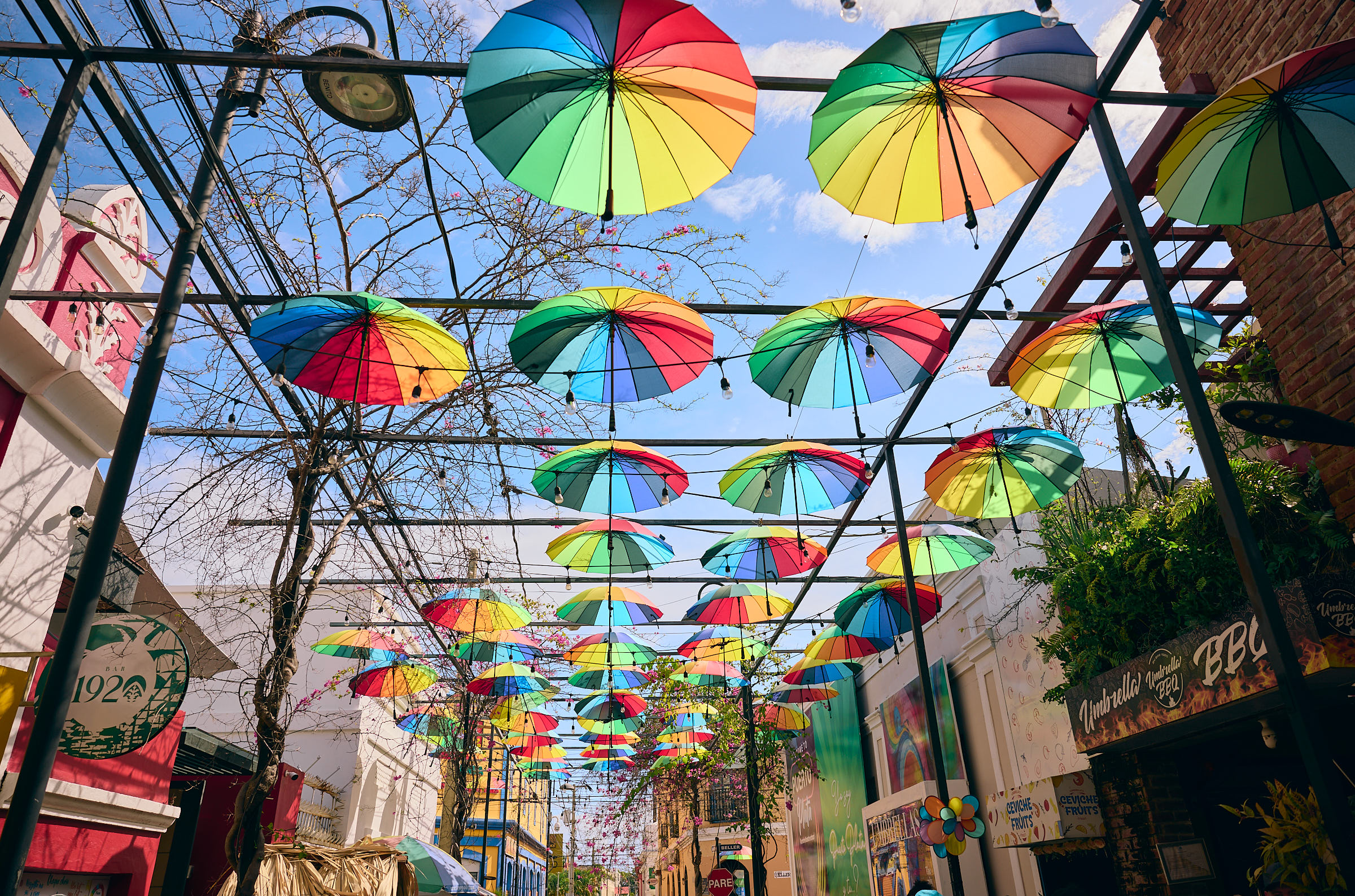 Alley with dozens of rainbow umbrellas suspended in the air