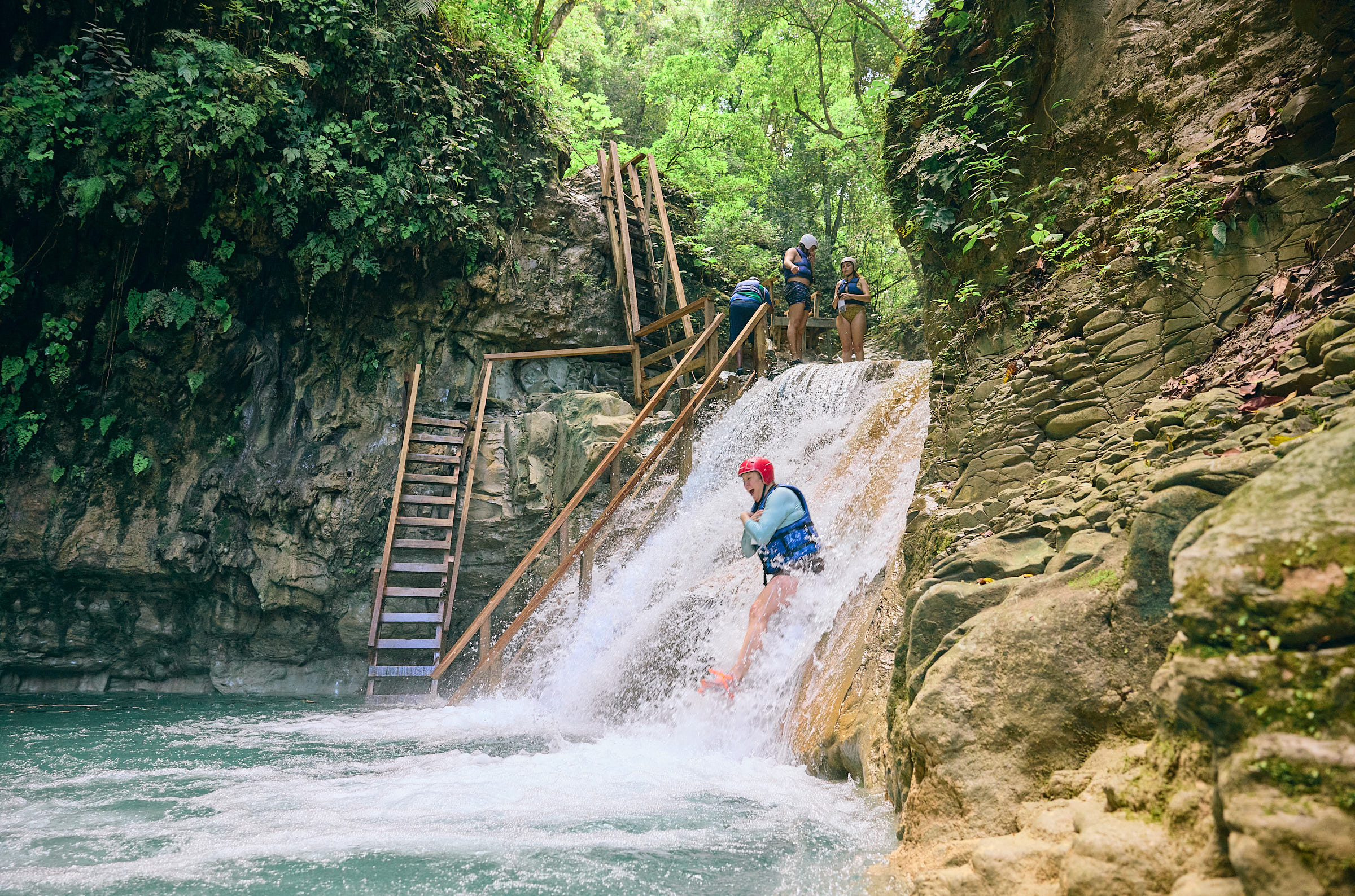 Woman sliding down a smooth rocky waterfall with her arms crossed