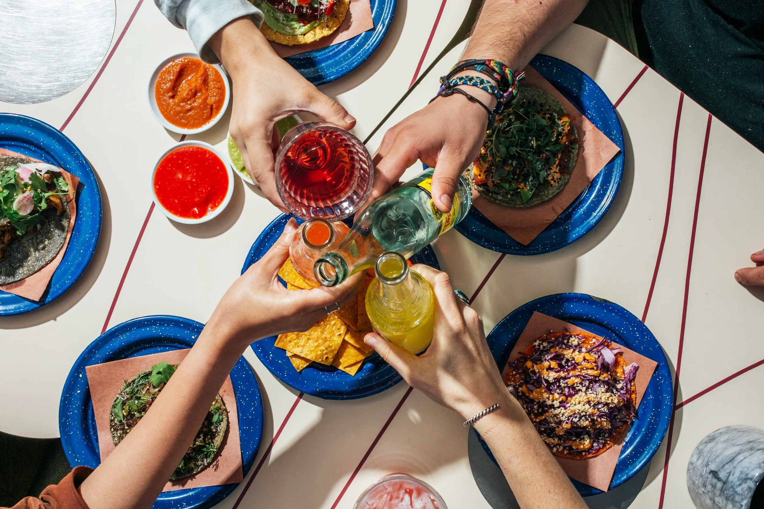 Overhead view of four hands toasting their drinks over a table with assorted Mexican food