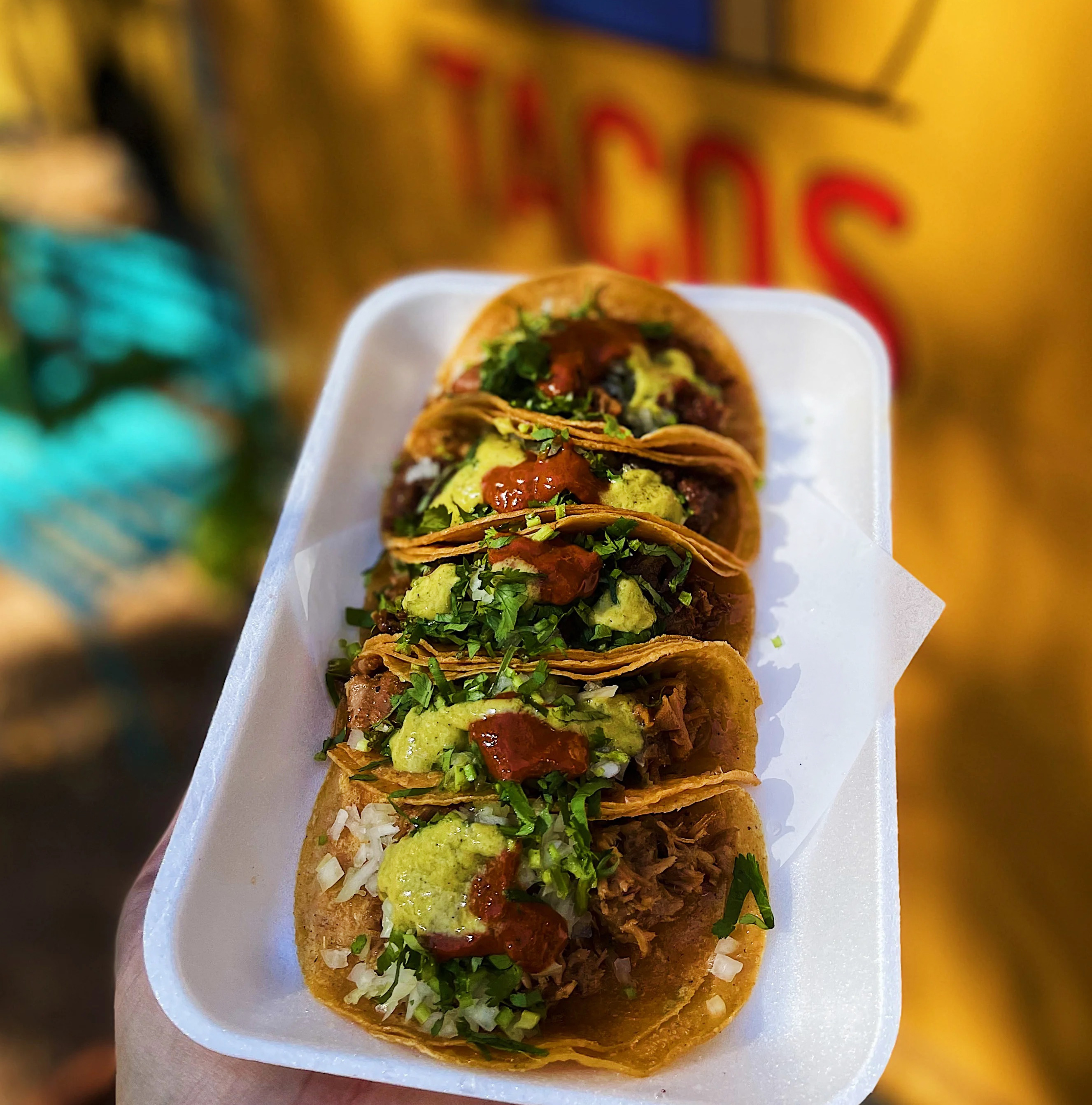 Five carnitas tacos stacked beside each other on a white tray