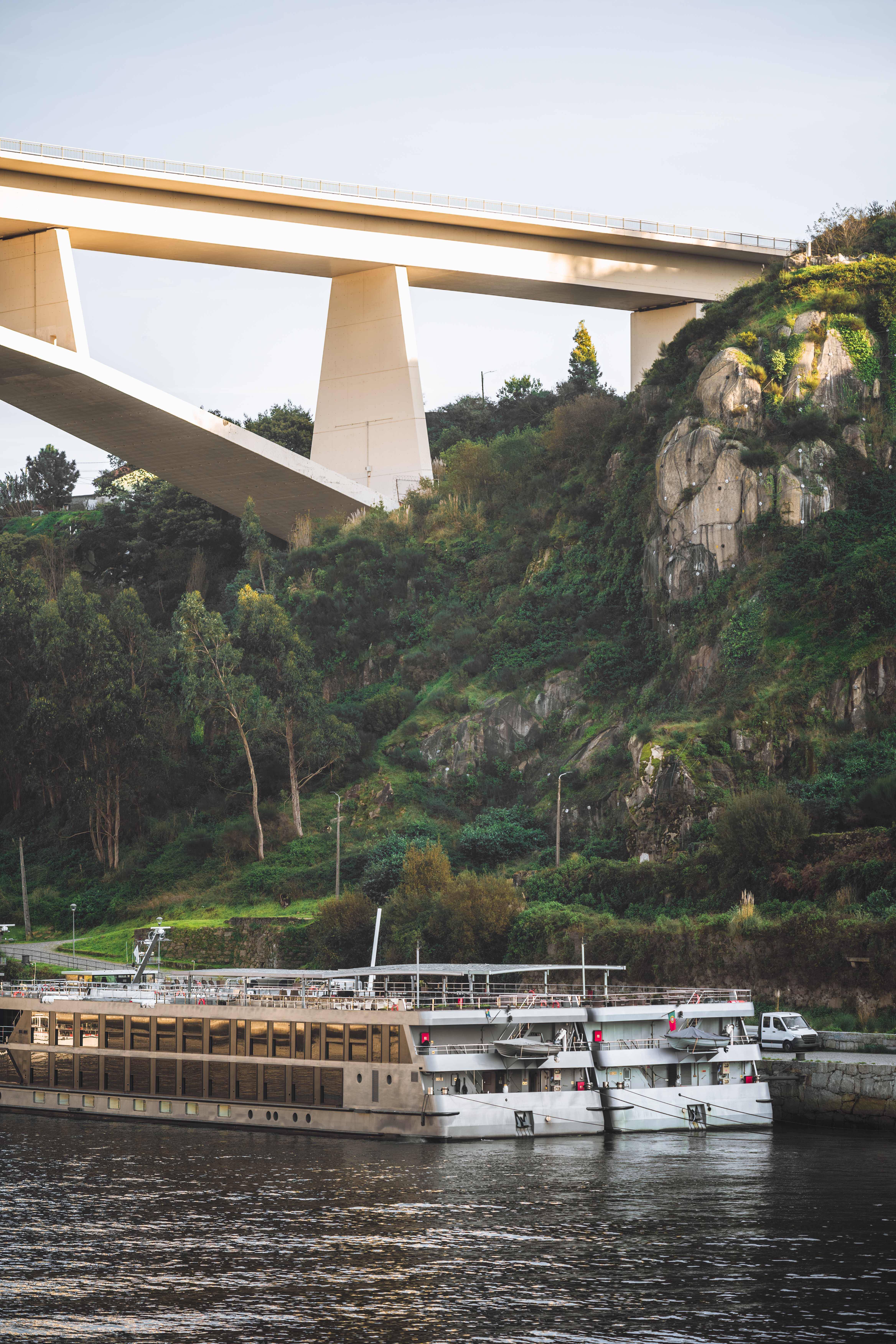 A river cruise ship is docked behead a large bridge