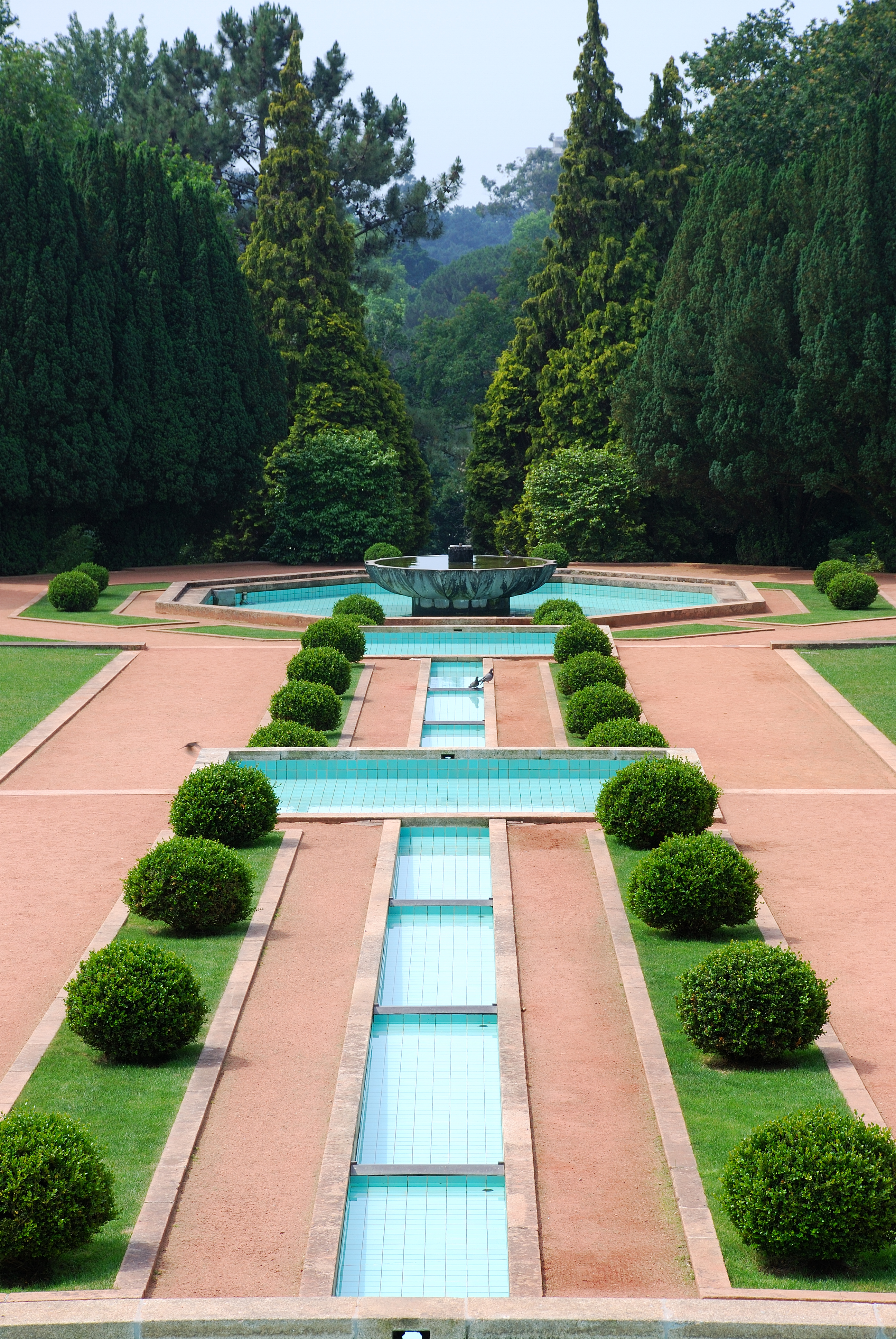 Circular boxwood hedges line stone paths and water fountains in a manicured garden